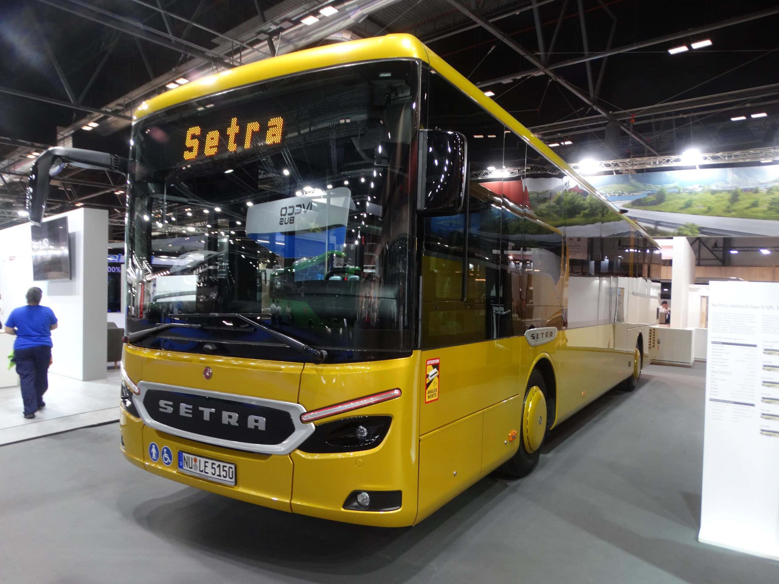 En una Feria Internacional, un autobús Setra amarillo se exhibe de forma impresionante en el interior, atrayendo la atención de los entusiastas del transporte.