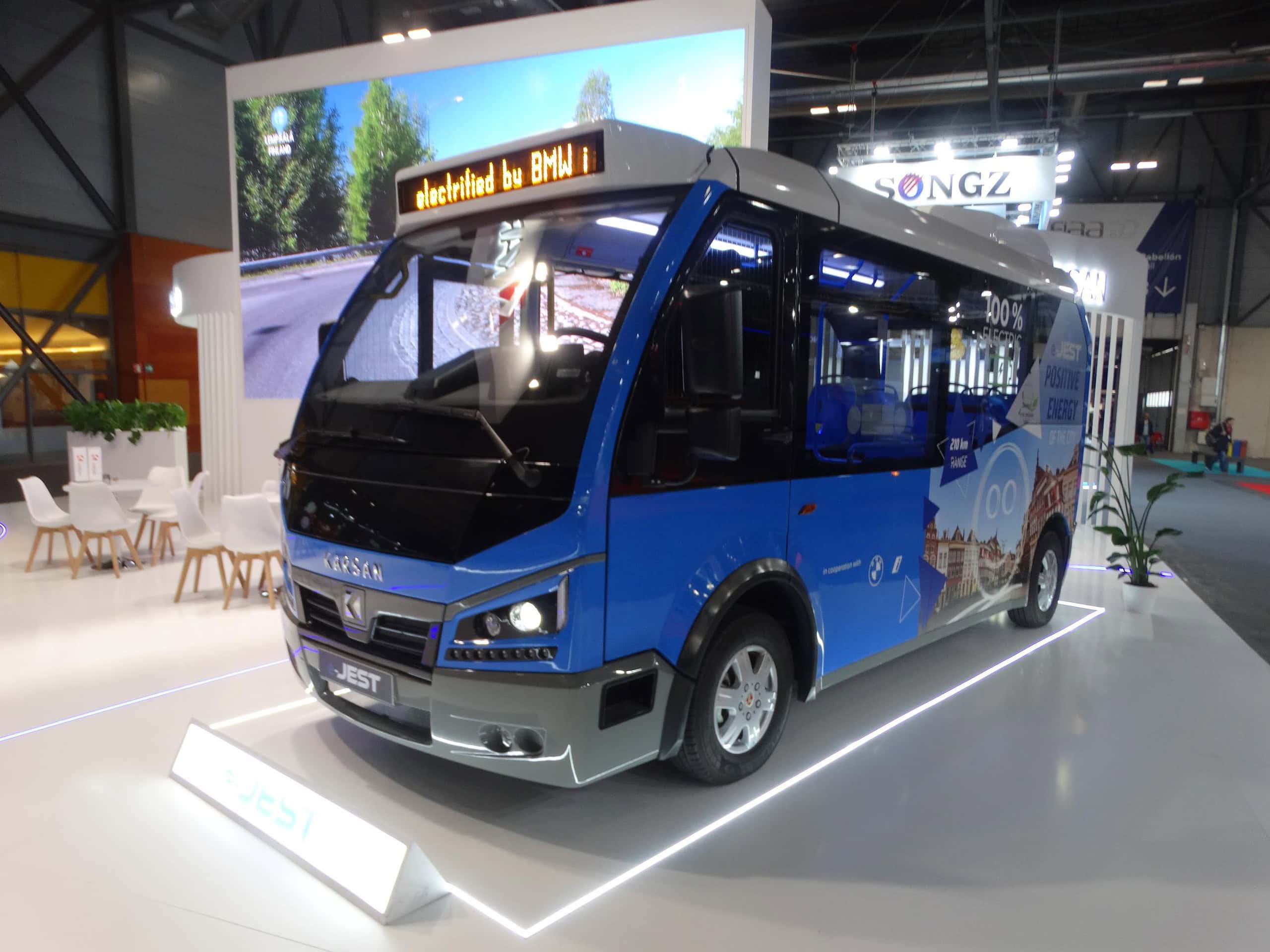 En la Feria Internacional del Autobús, los visitantes admiraron un minibús eléctrico azul expuesto en una exposición interior, con sus laterales adornados con llamativos gráficos promocionales.