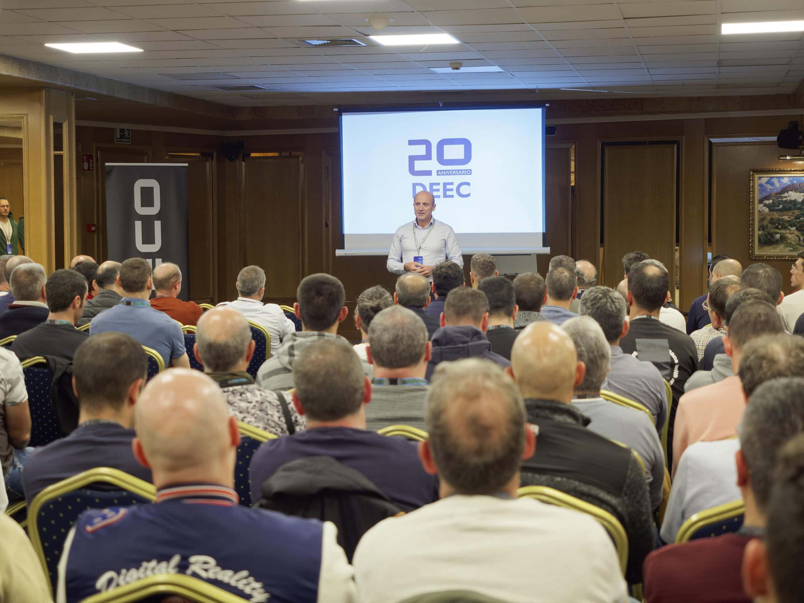Un hombre se dirige a un público sentado en una sala de conferencias, donde una pantalla muestra "20 DEEC" de fondo. El evento forma parte de un programa de formación de IVECO centrado en el diagnóstico de camiones, cuyo objetivo es mejorar los conocimientos y las habilidades técnicas de la industria.