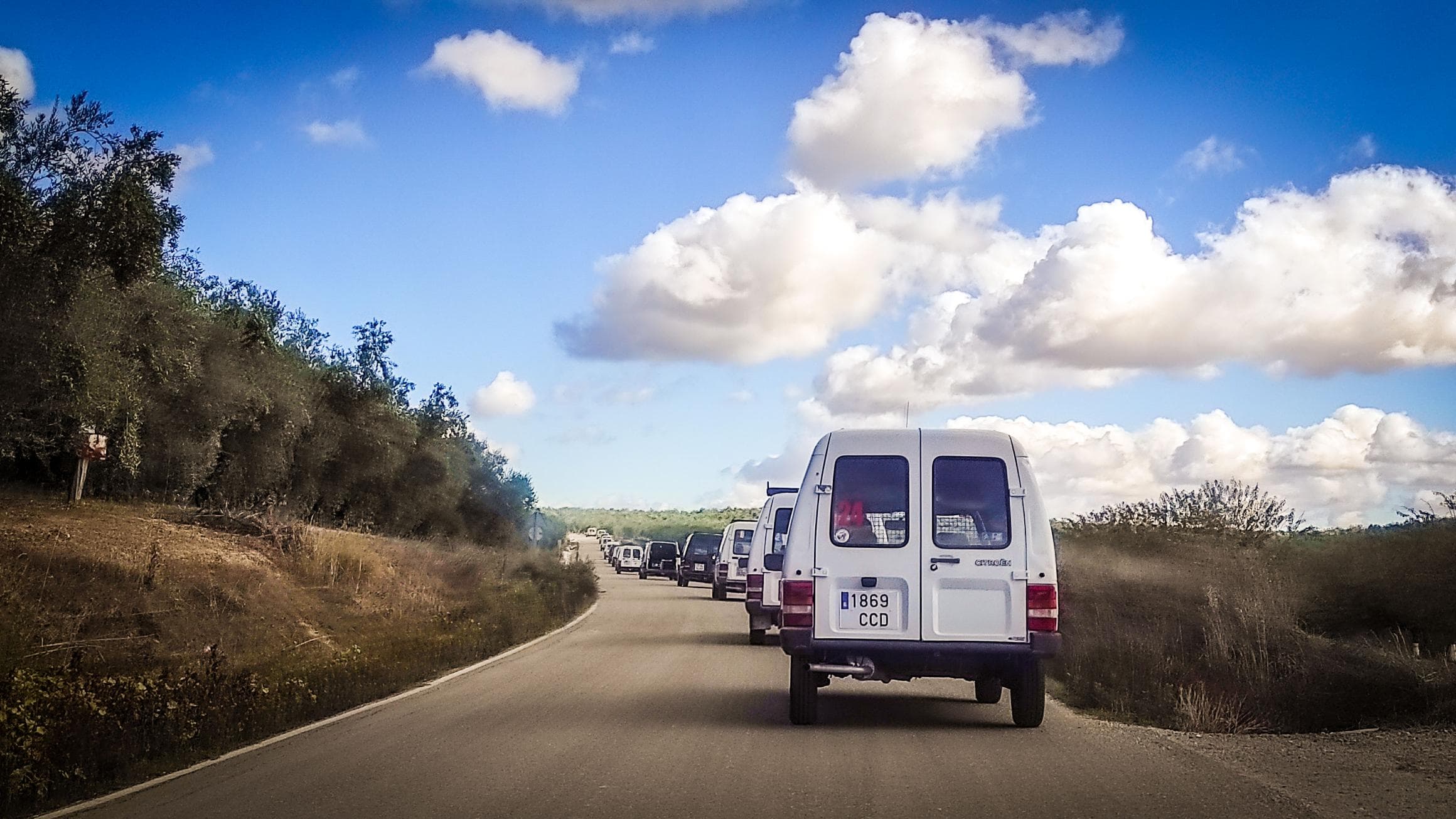 Un convoy de furgonetas blancas Citroën C-15 avanza por una carretera rural bajo un cielo azul con nubes, que recuerda a una expedición a Marruecos.