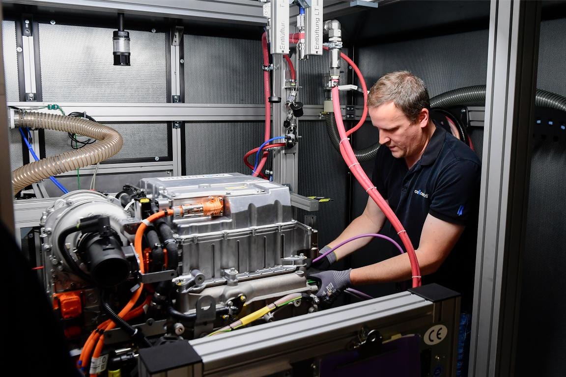 En un entorno de laboratorio de alta tecnología, un hombre trabaja con equipos con cables de diversos colores, concentrándose intensamente en mejorar la eficiencia de los camiones eléctricos.