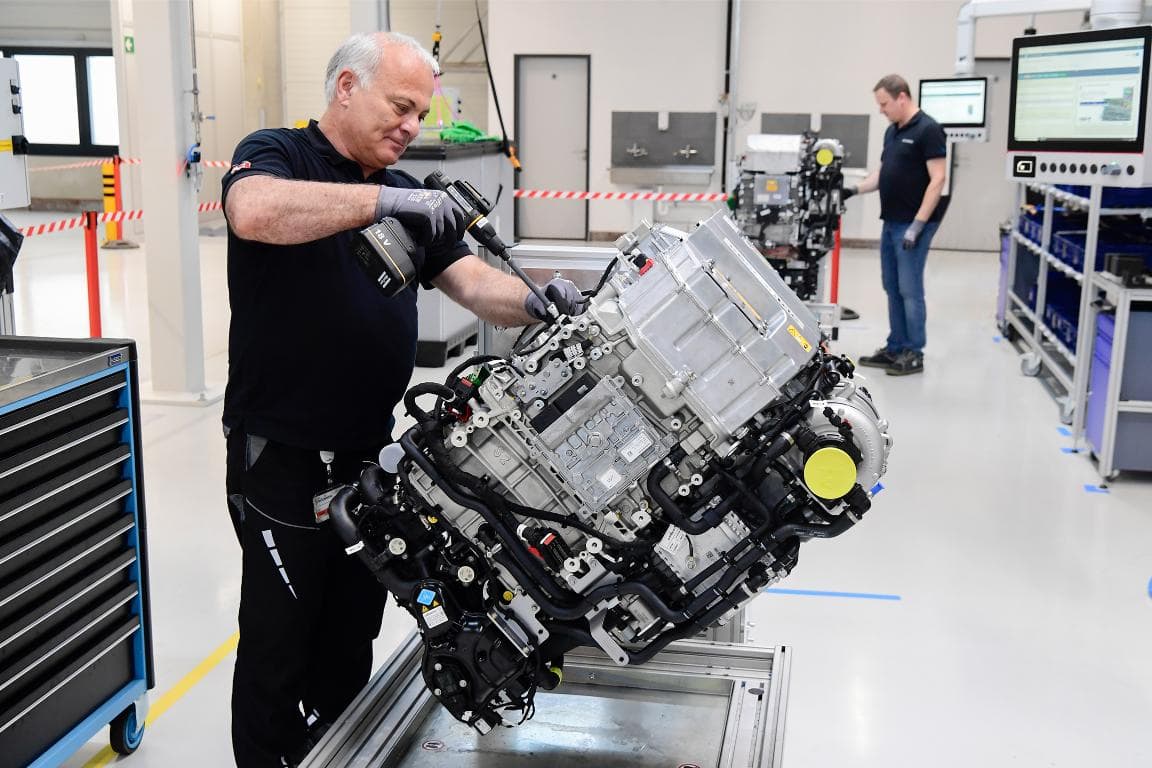 Un técnico ensambla meticulosamente un motor en un taller, mientras otra persona trabaja diligentemente en segundo plano, asegurándose de que los camiones eléctricos estén alimentados por baterías de primera línea para un rendimiento máximo.