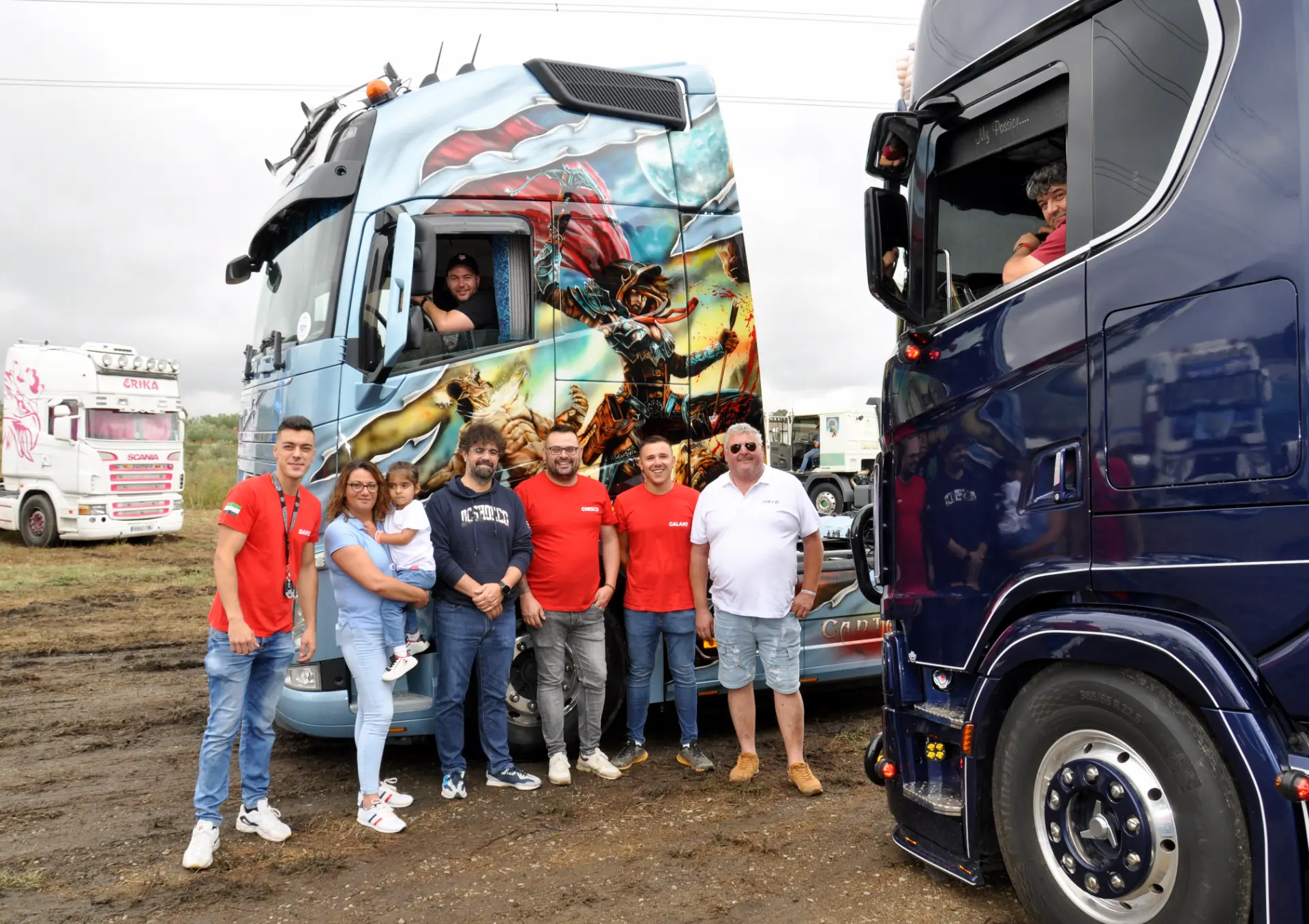 Un grupo de personas se encuentra de pie frente a camiones decorados, algunos con camisetas rojas, reunidos en un evento de camiones. Entre la multitud, se podía ver un "borrador automático" exhibido con orgullo en uno de los parabrisas del camión, mostrando innovación junto con tradición.