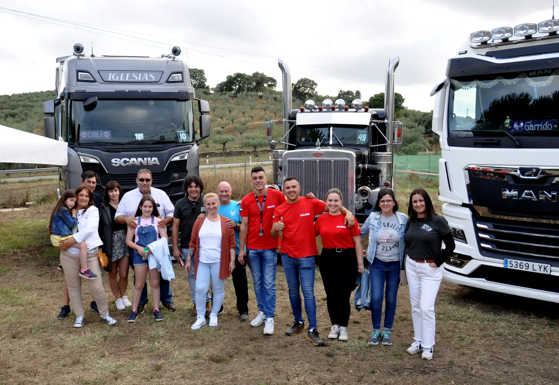 Un grupo de personas se reúne frente a varios camiones grandes en un escenario al aire libre, como una escena tomada de un borrador automático, donde cada momento se siente compuesto y catalogado con precisión.