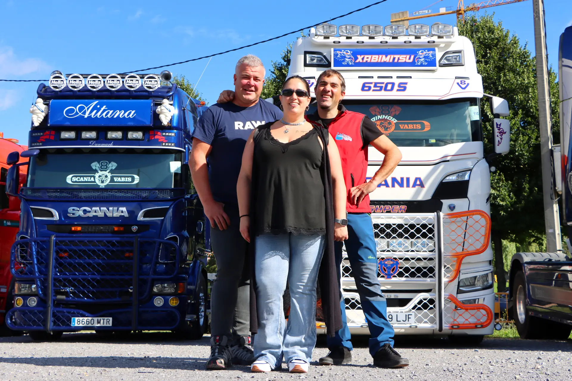Tres personas sonriendo delante de dos camiones Scania decorados en un día soleado en el animado Festival de Camiones de Barakaldo.