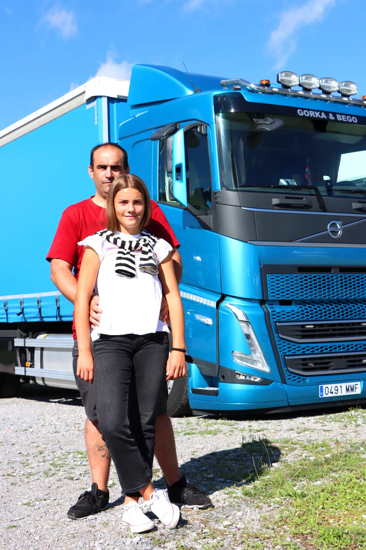 En un día soleado, un hombre y una niña permanecen orgullosos delante de un gran camión azul en el Festival de Camiones de Barakaldo.