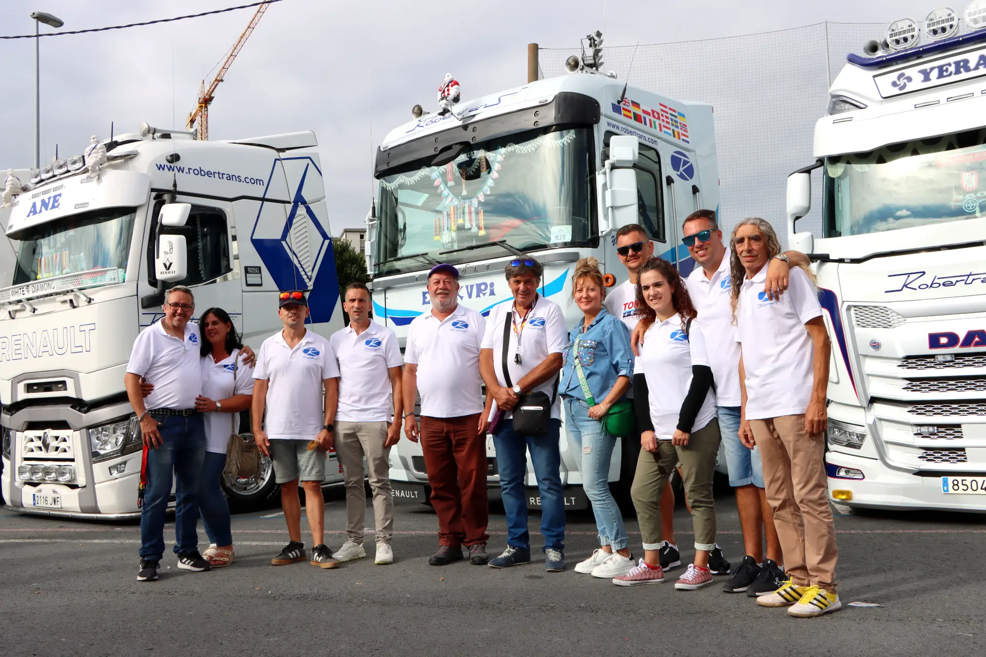 Un grupo de personas con camisa blanca se reúne, unidas por el entusiasmo, posando orgullosas delante de los camiones decorados en un día nublado en el Festival de Camiones de Barakaldo.