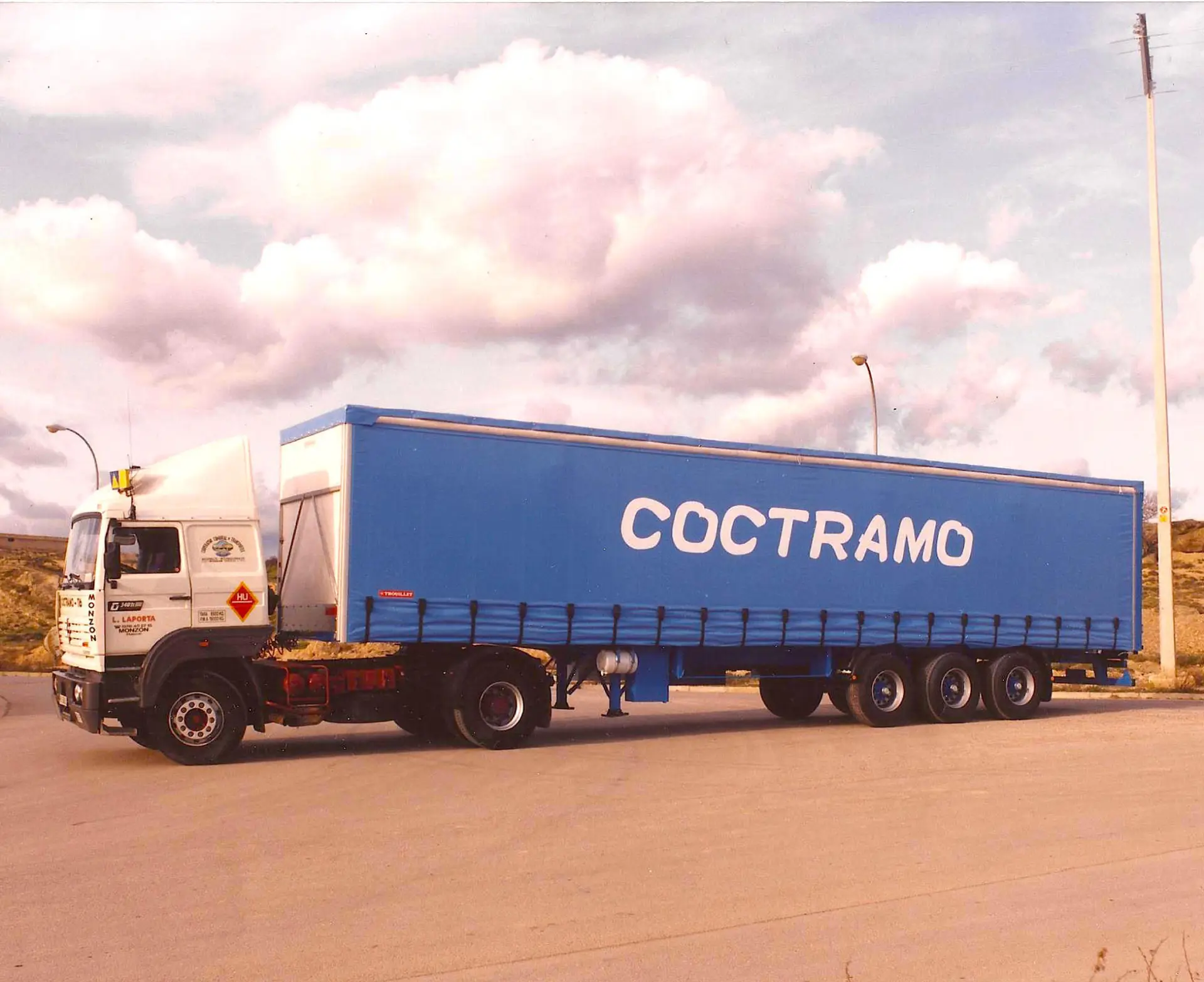 Un camión COCTRAMO azul con remolque, propiedad de Antonio Plata, está estacionado en una carretera bajo un cielo nublado cerca de Sevilla.