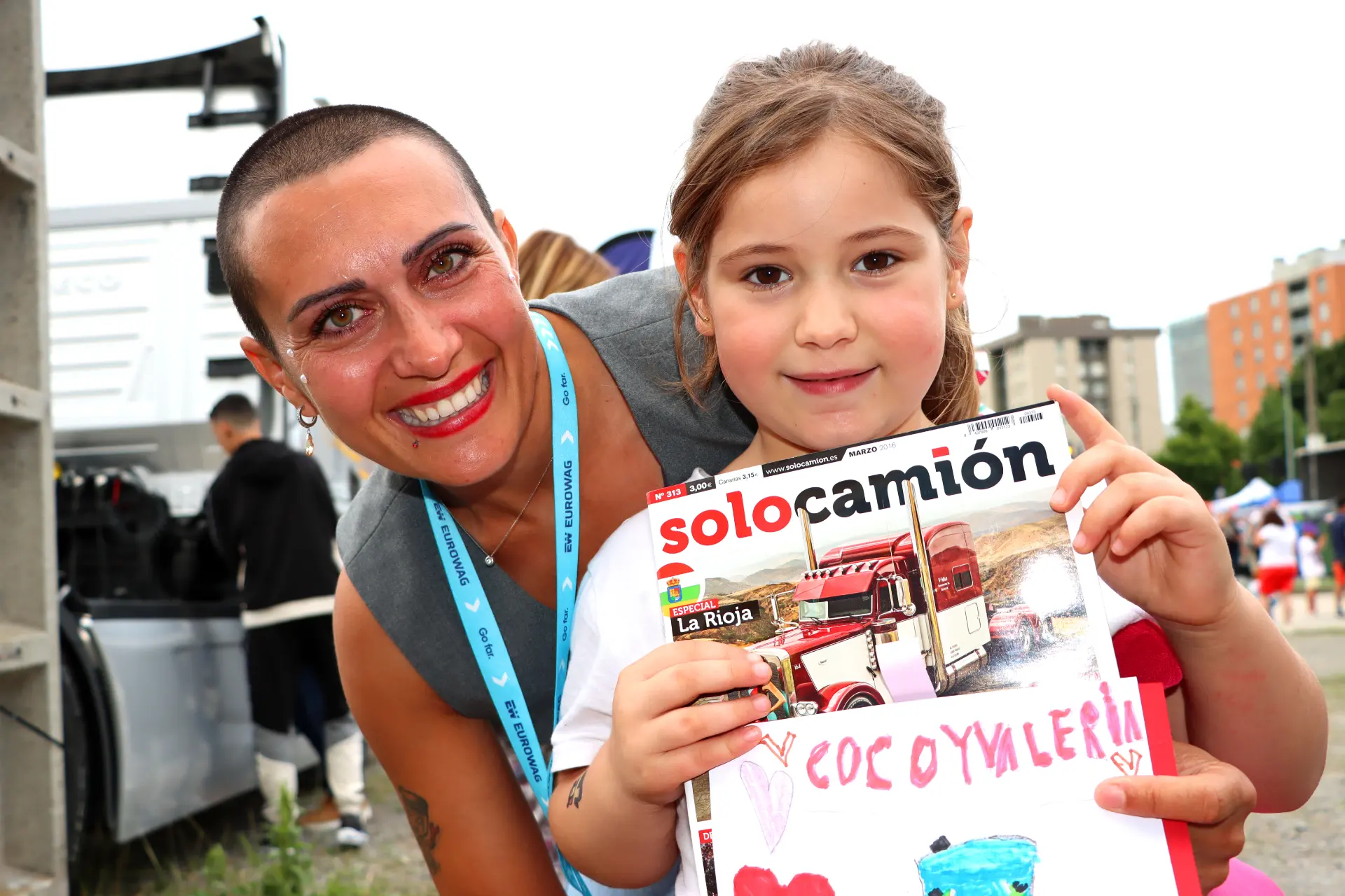 Una mujer sonriente con un cordón y una niña sosteniendo un puesto de la revista "Solo Camión" en el exterior, encarnan el espíritu que se respira en el Festival del Camión de Barakaldo.