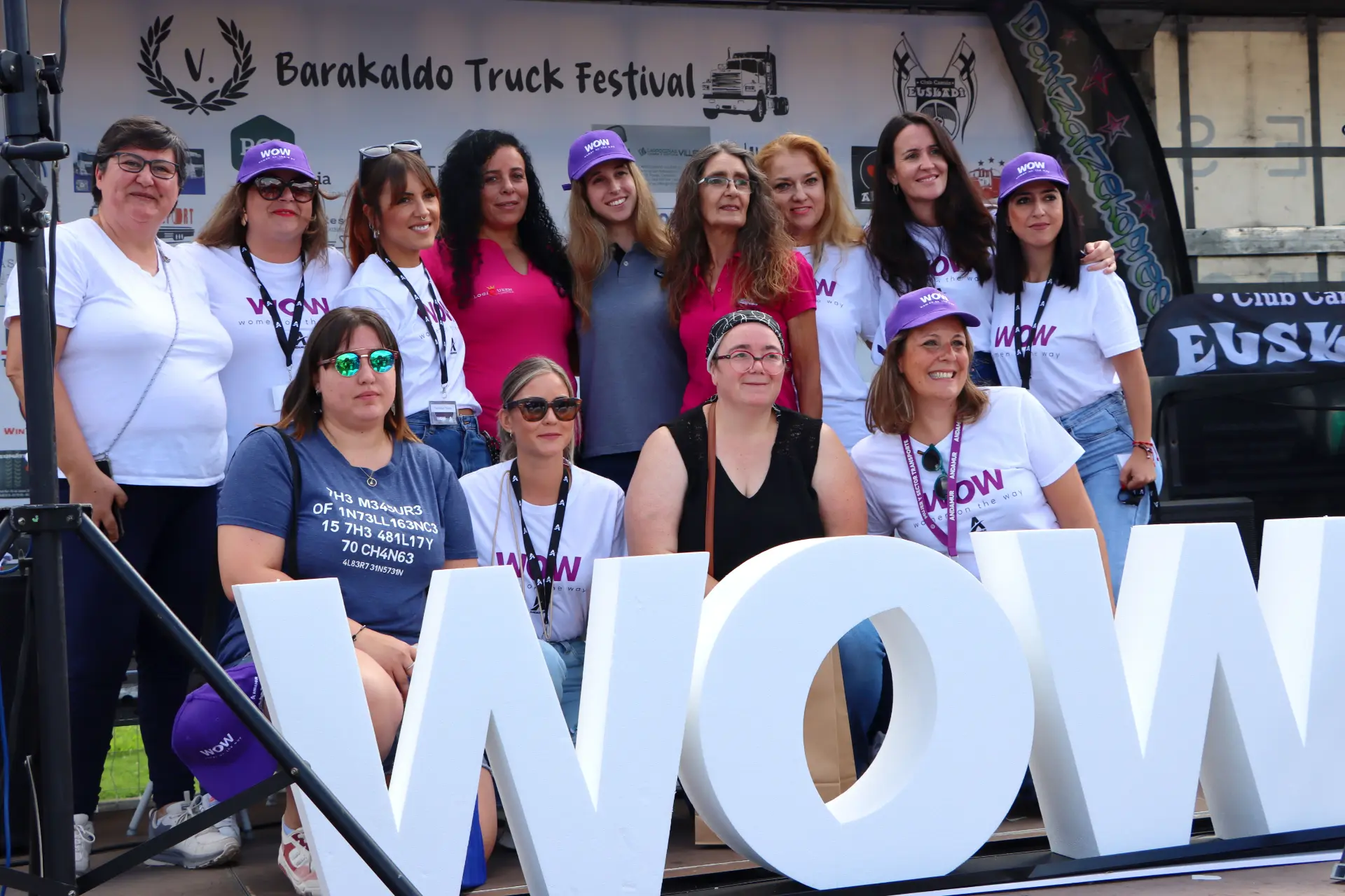 Un grupo de mujeres posa alegremente juntas en el V Festival de Camiones de Barakaldo, de pie orgullosamente detrás de grandes letras "WOW" en el escenario.