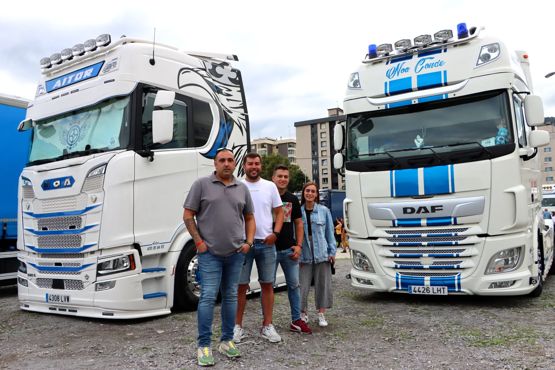 Un grupo de cuatro personas se sitúa entre dos grandes camiones blancos en un aparcamiento durante el Festival de Camiones de Barakaldo.