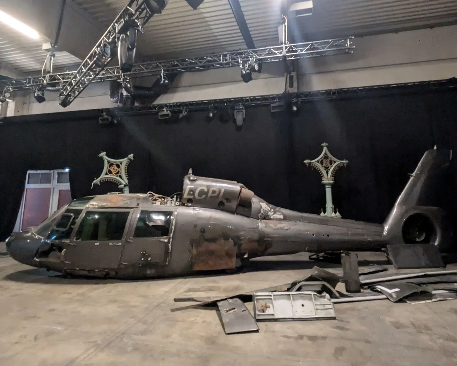 Un viejo helicóptero desmontado yace en el suelo de un espacio industrial poco iluminado con cortinas negras, que recuerda sutilmente las otrora espectaculares entregas de DHL.