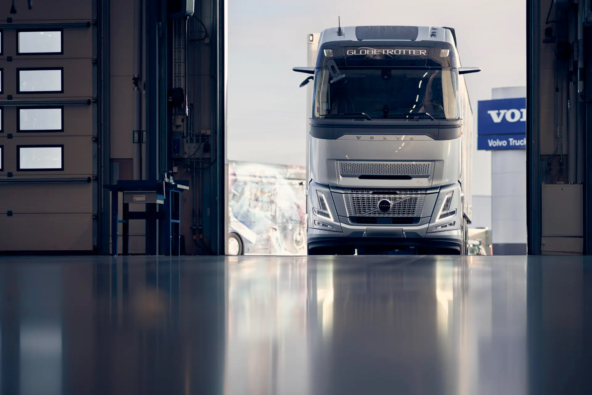 El camión Volvo FH Aero de color blanco se ve parcialmente, estacionado dentro de un garaje con la puerta abierta. Conocido por sus características de ahorro de combustible, este modelo representa eficiencia y diseño moderno incluso cuando está parado.