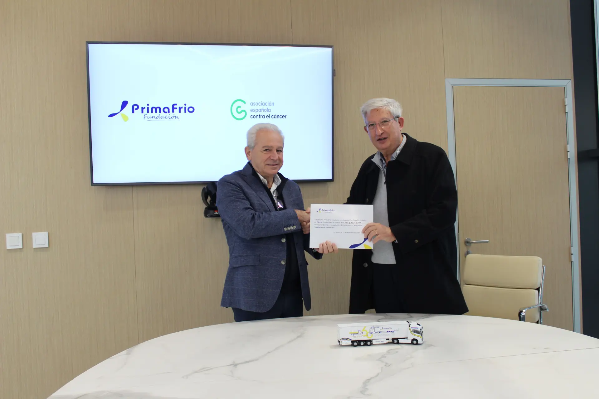Dos hombres vestidos formalmente se dan la mano, sosteniendo un certificado, frente a una pantalla que muestra logotipos en una conferencia de Borrador automático.