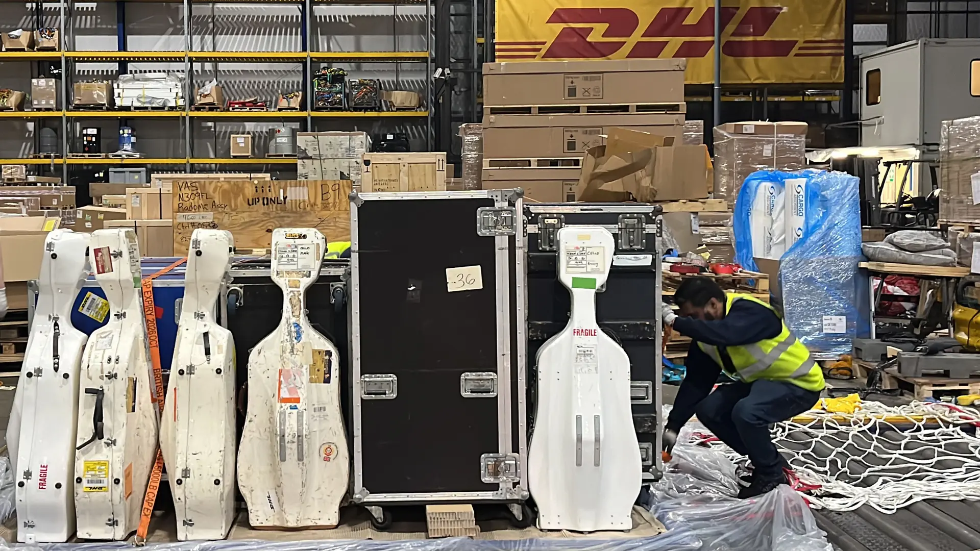 Un trabajador clasifica eficientemente cajas y paquetes en un almacén lleno de actividad con una destacada pancarta de DHL en el fondo, garantizando entregas sin problemas para 2024.