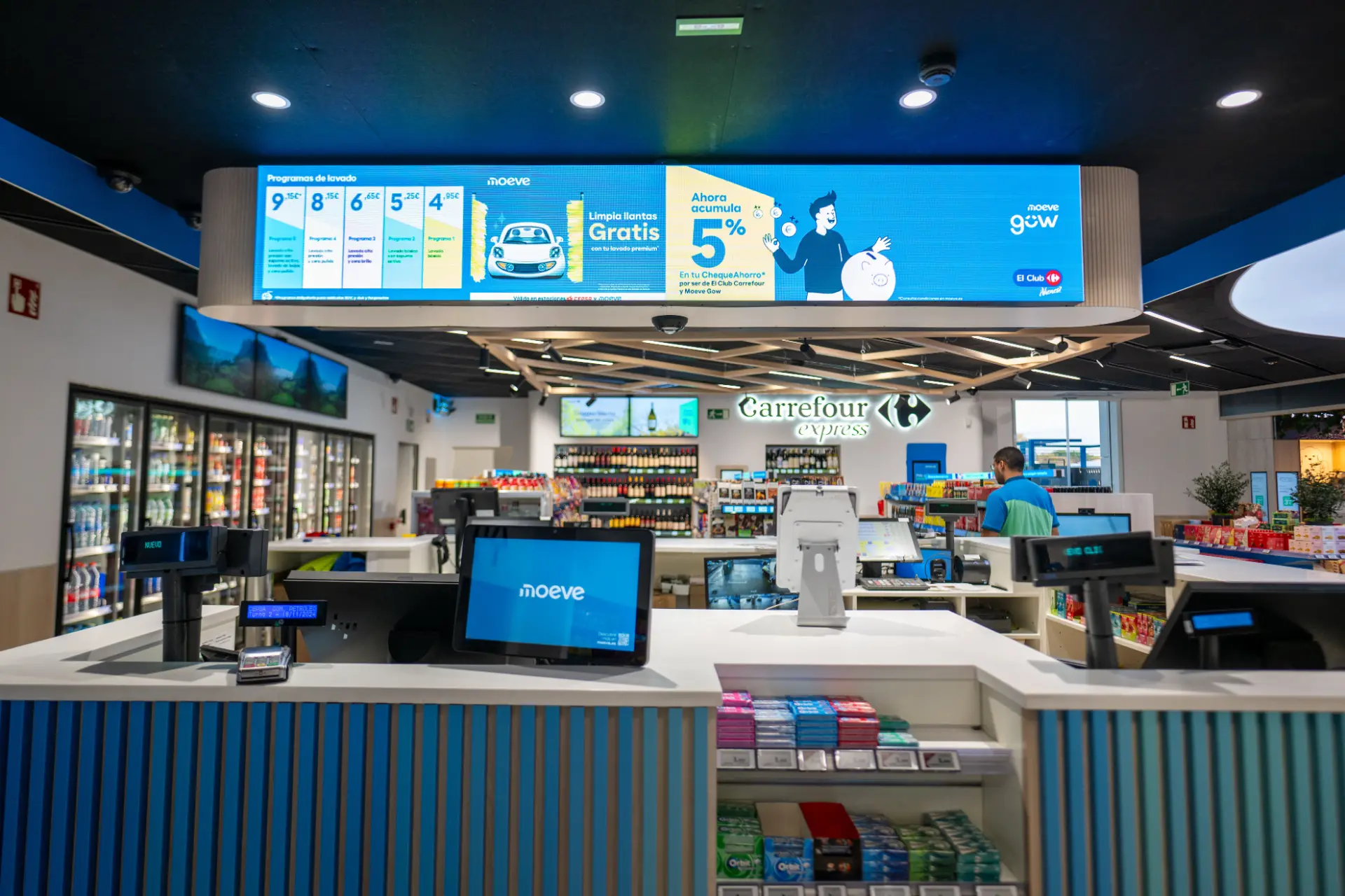 El interior de una tienda Carrefour Express presenta mostradores de caja y pantallas promocionales que revolucionan la experiencia de compra, como las innovadoras estaciones Moeve.
