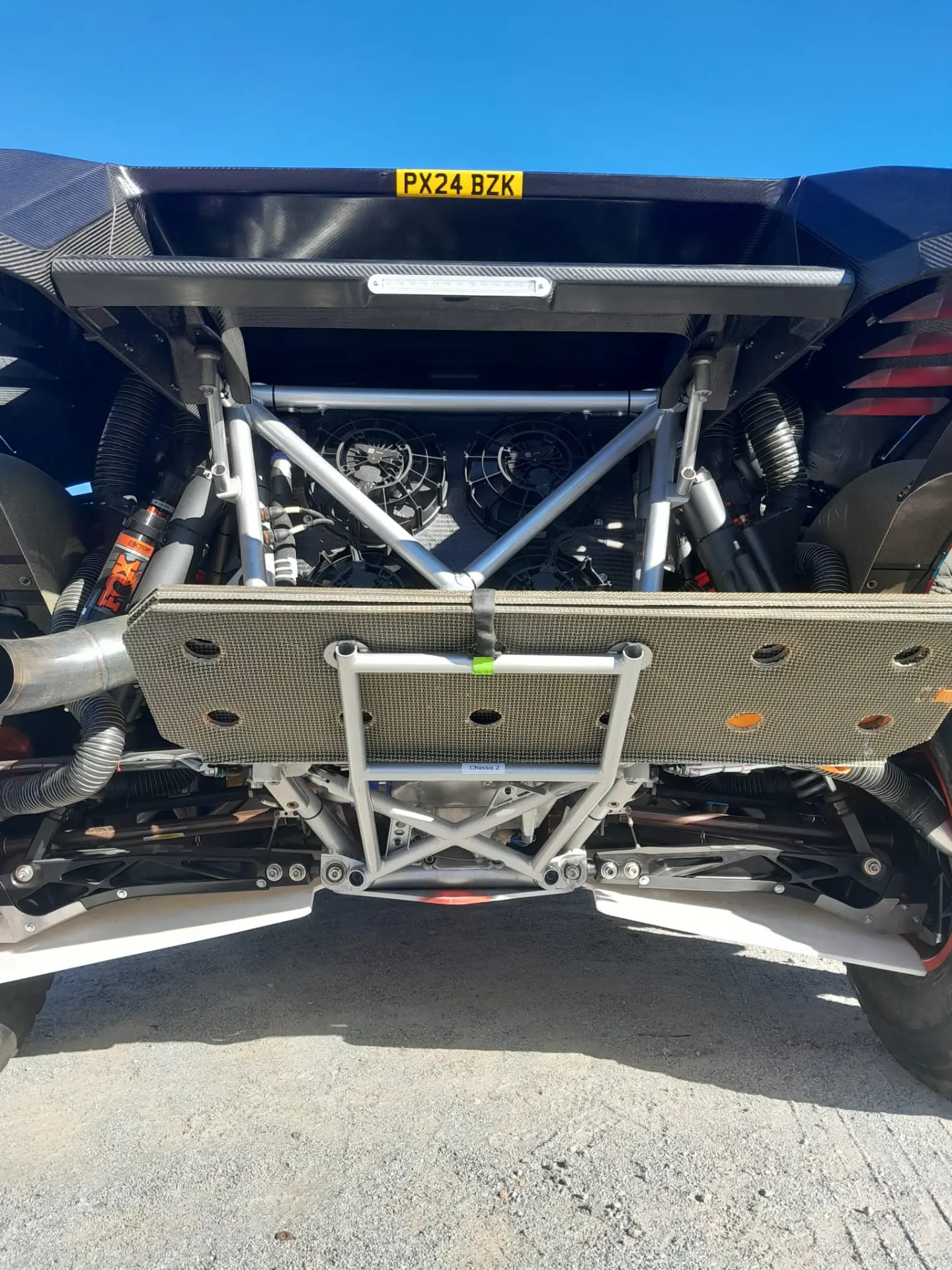 Una vista trasera de un chasis de automóvil elegante y de alto rendimiento, que recuerda al Ford Raptor T1+, muestra una suspensión visible y ventiladores de refrigeración, que encarnan el espíritu de las aventuras del Dakar 2025.