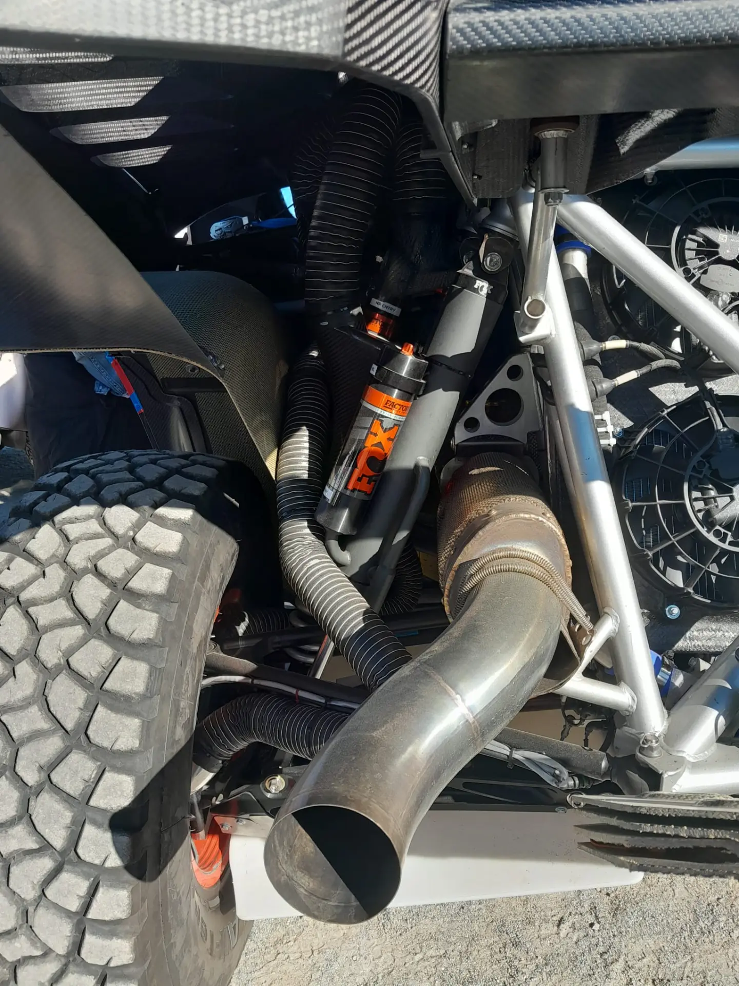 Primer plano de un robusto sistema de suspensión todoterreno Ford Raptor con un neumático, un amortiguador y un tubo de escape visibles, que recuerda a las robustas construcciones vistas en Dakar 2025 y conducidas por leyendas como Carlos Sainz.