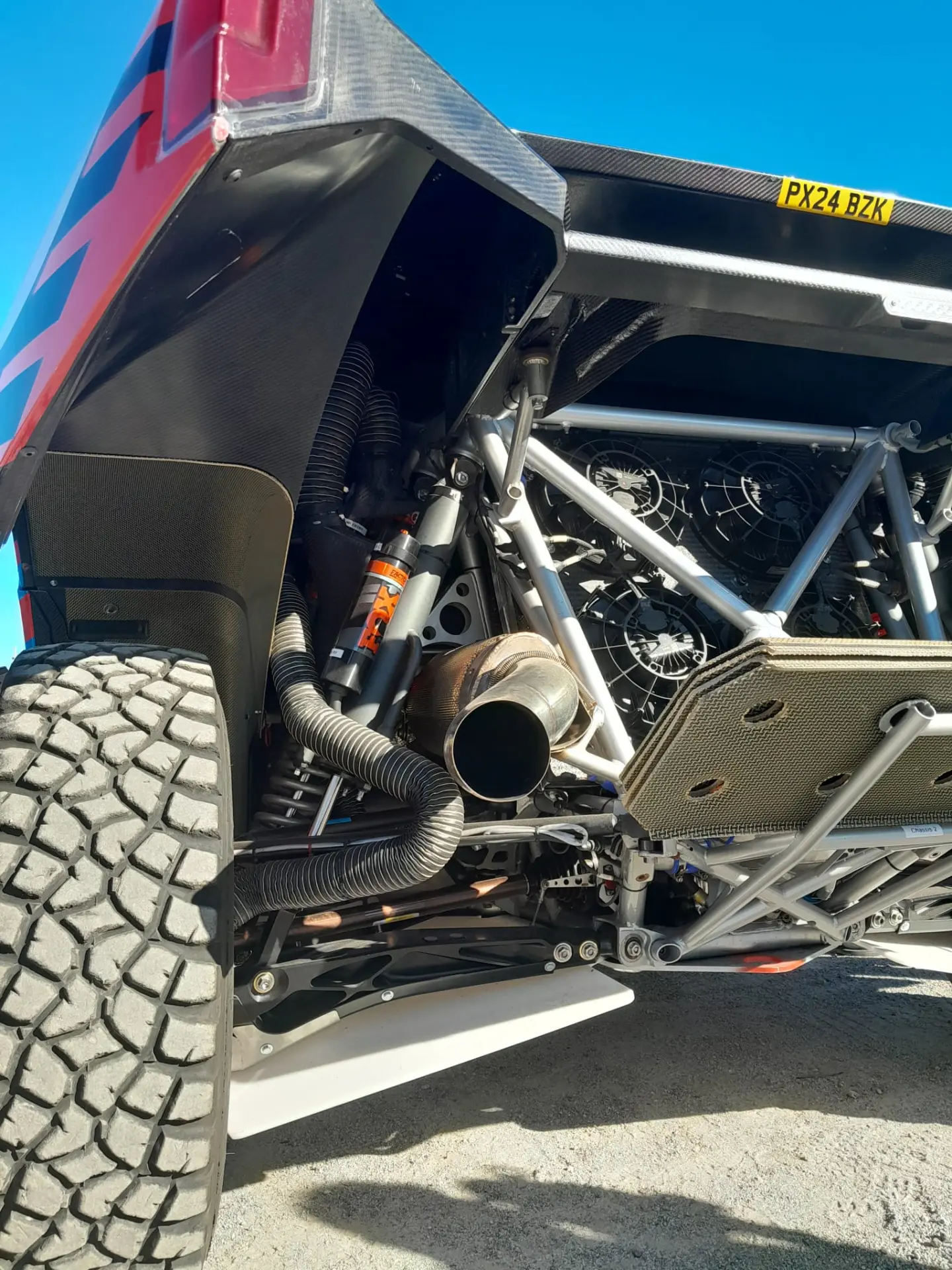 Primer plano de la suspensión y el sistema de escape de un robusto vehículo todoterreno, resaltando los neumáticos grandes y el marco de metal, que recuerdan la excelencia de ingeniería observada en el Ford Raptor.