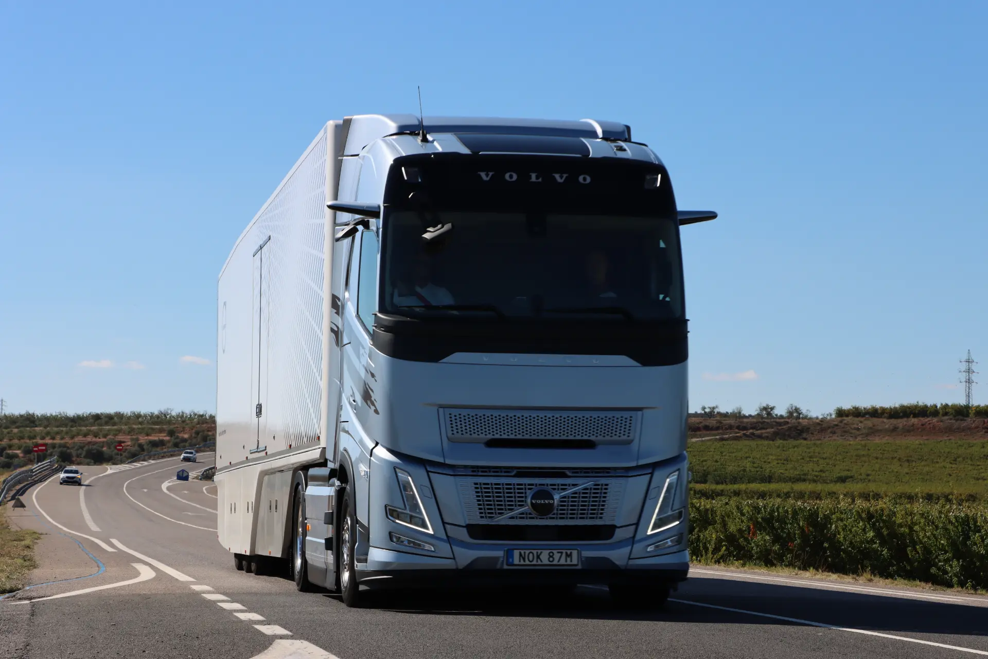 Un elegante camión Volvo FH plateado avanza por la autopista, mejorado con tecnología I-Save, contra un fondo de cielo azul claro.