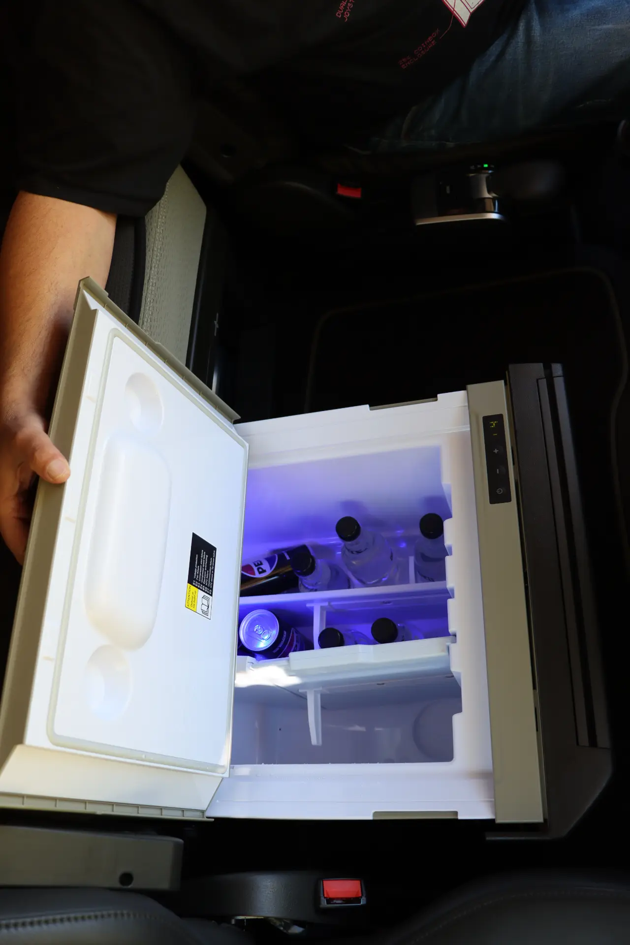 Una persona abre el pequeño refrigerador del automóvil lleno de bebidas embotelladas, cuyo contenido está iluminado por una fría luz azul, que recuerda al diseño eficiente que encontramos en un Volvo FH con tecnología I-Save.