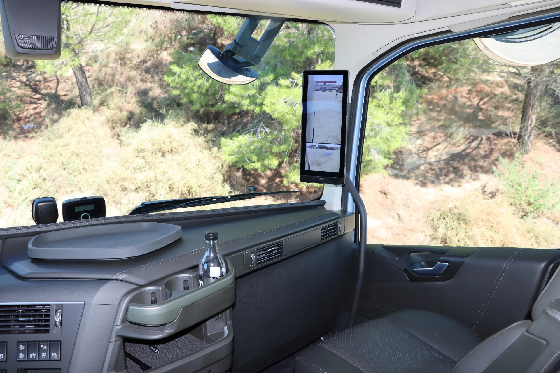 El interior de la cabina del camión Volvo FH cuenta con una elegante pantalla digital que enmarca perfectamente el frondoso paisaje de árboles del exterior. Con la tecnología I-Save, este modelo Aero 460 garantiza un viaje eficiente y sereno a través de la belleza de la naturaleza.