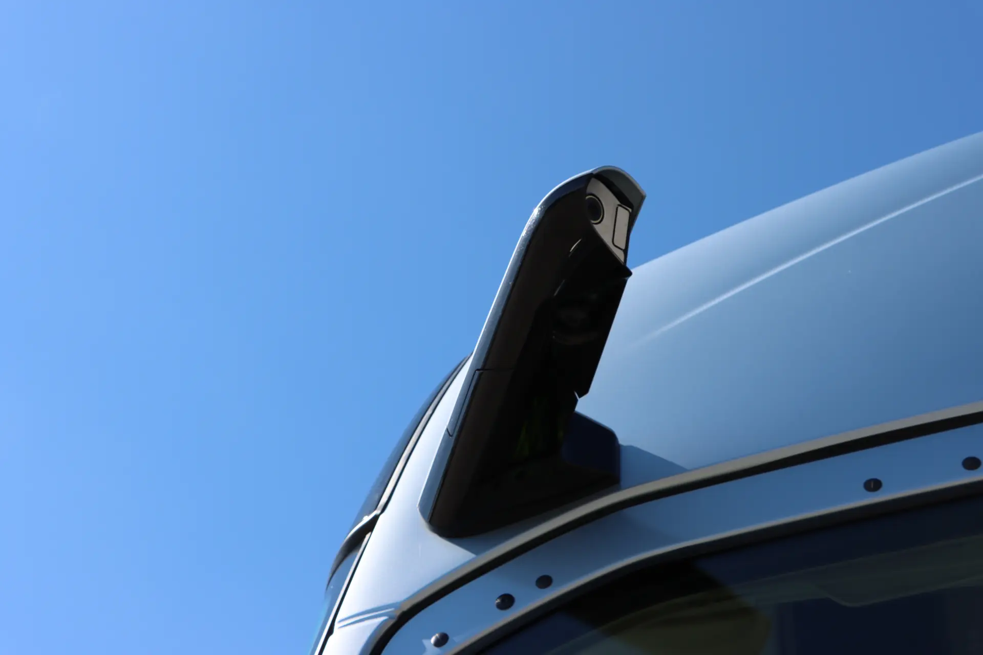 Primer plano de una cámara de espejo lateral en un Volvo FH con diseño Aero 460, frente a un cielo azul claro.