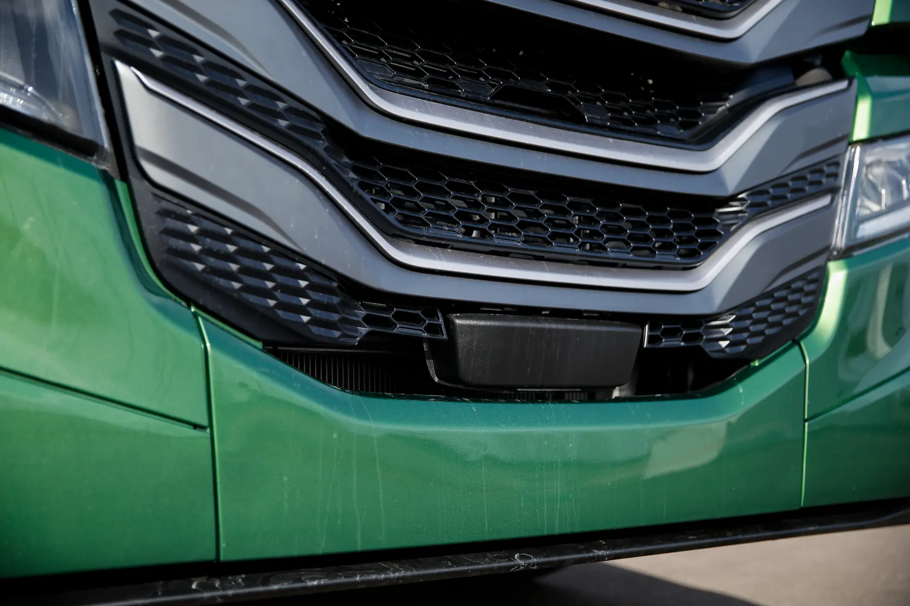 Primer plano de la parrilla de un vehículo Iveco verde con detalles de ventilación en negro y gris, que muestra los elementos de diseño distintivos del modelo MY24.