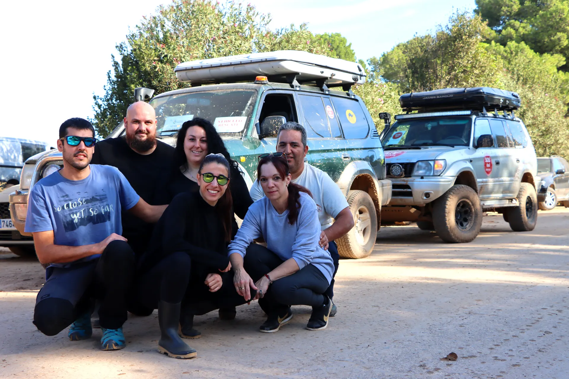 Un grupo de seis personas posa frente a dos vehículos todoterreno en un camino de tierra, rodeado de árboles, capturando el espíritu aventurero del sector de transporte de Dana.