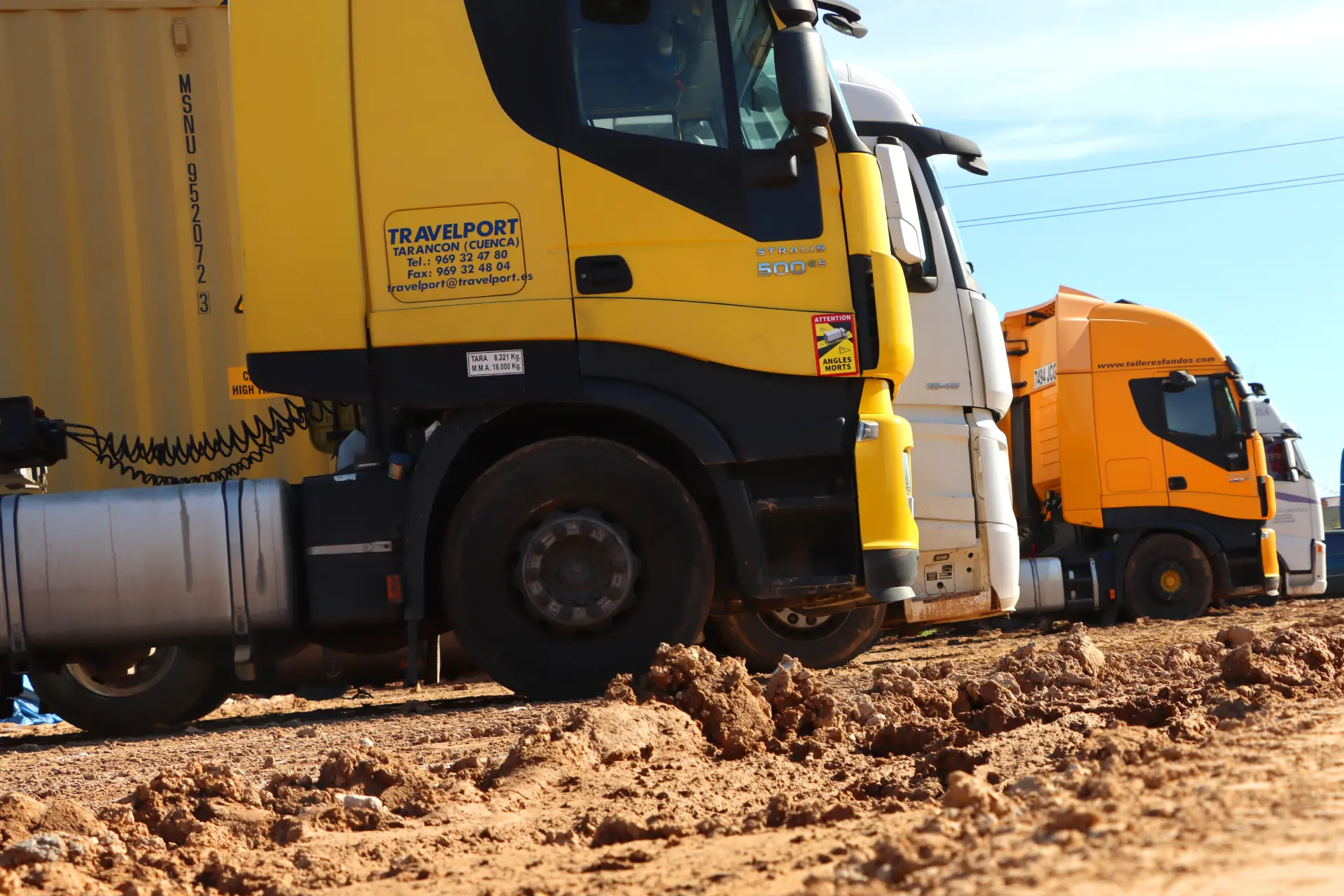 Bajo un cielo azul claro, varios camiones amarillos están estacionados en un lote de tierra, pintando una imagen vívida del dinámico sector del transporte.
