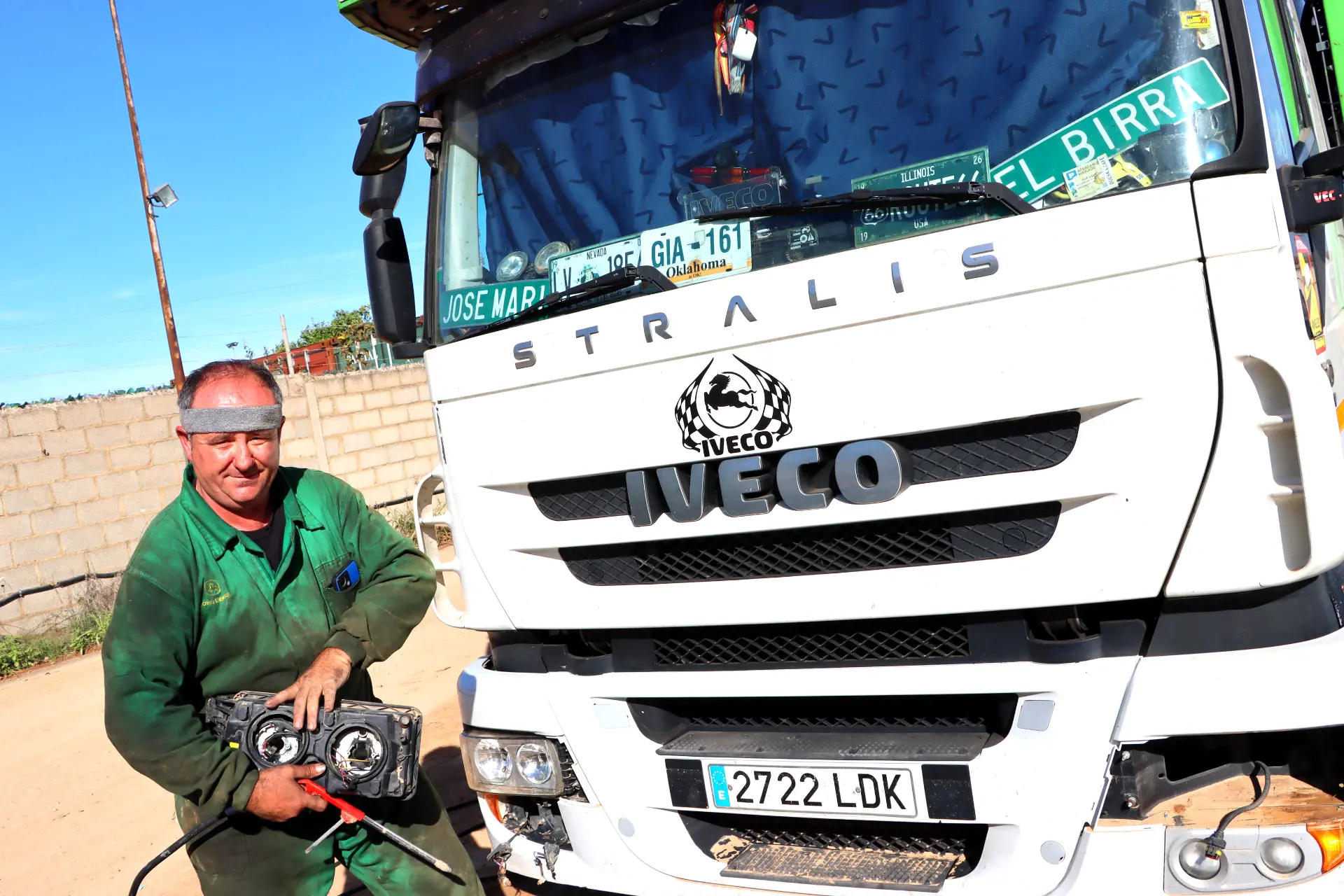Un hombre con un mono verde se encuentra junto a un camión Iveco, sosteniendo herramientas, en un día soleado, listo para enfrentar cualquier desafío en el sector del transporte.