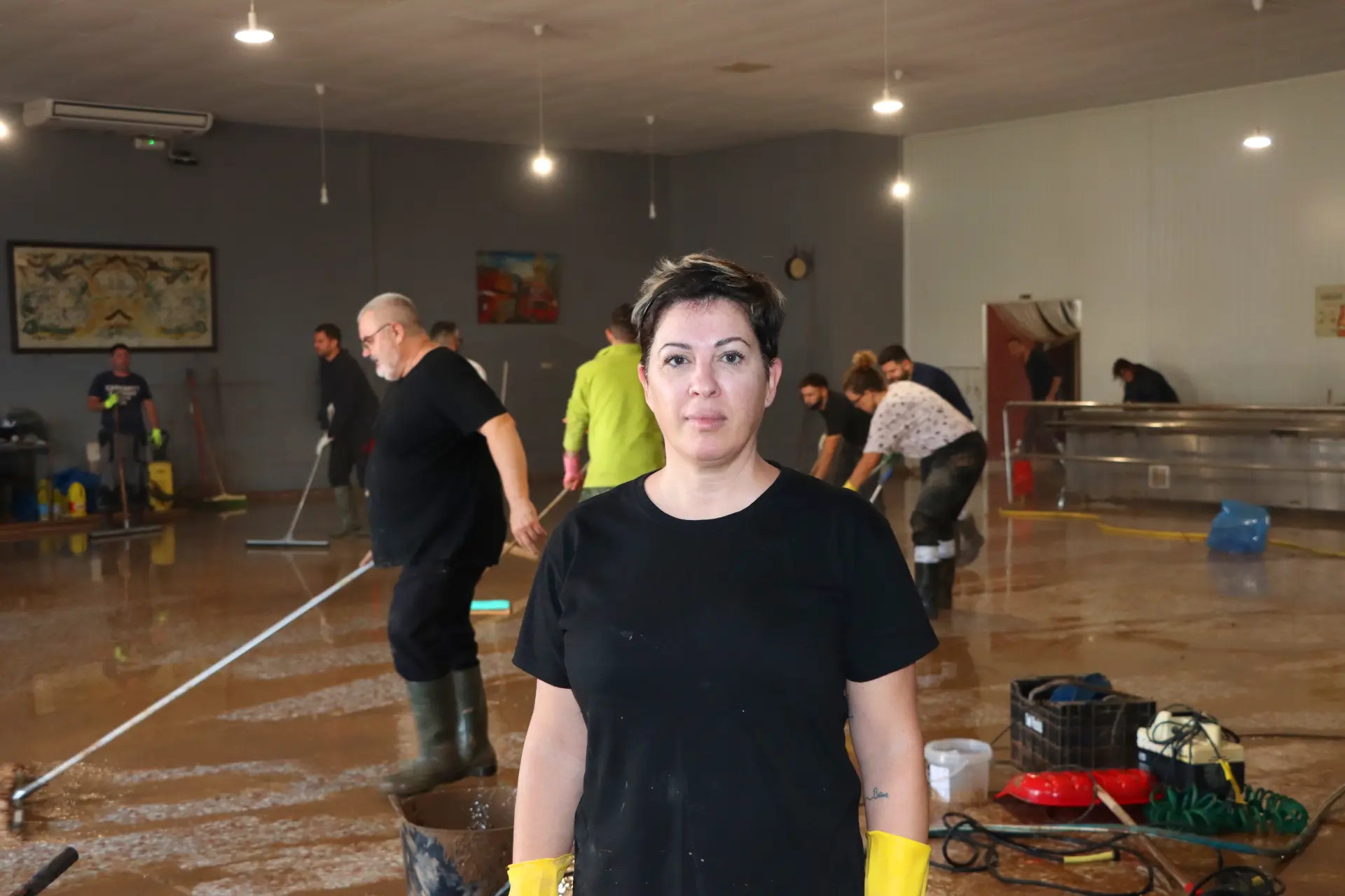 En el cuarto lleno de barro, Dana, una mujer de negro con guantes amarillos, se mantiene firme. Detrás de ella, otros del sector del transporte limpian diligentemente con escobas y trapeadores.