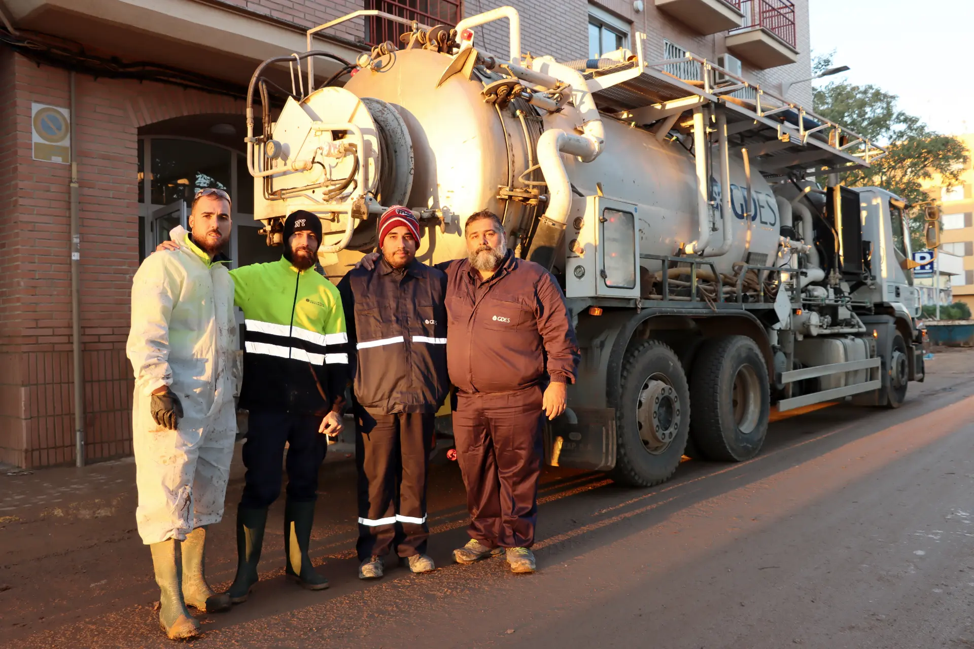 Cuatro trabajadores con ropa protectora se encuentran frente a un gran camión utilitario en una calle, listos para enfrentar cualquier desafío que se les presente en el sector del transporte.