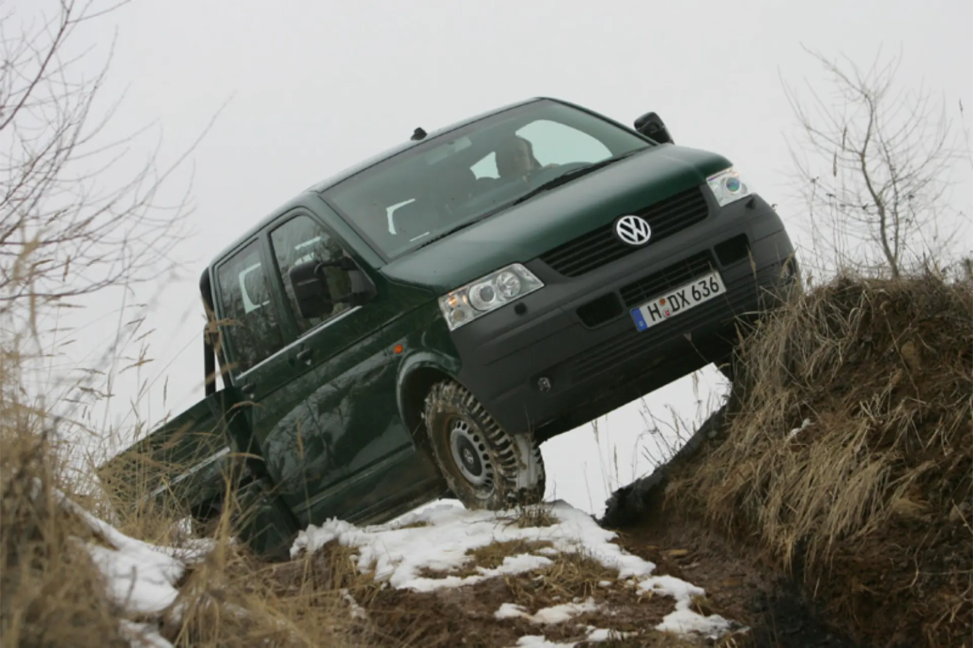 Una camioneta Volkswagen Vehículos Comerciales verde, que celebra 40 años de innovación, aborda la colina cubierta de hierba y nieve con facilidad gracias a su tracción total.