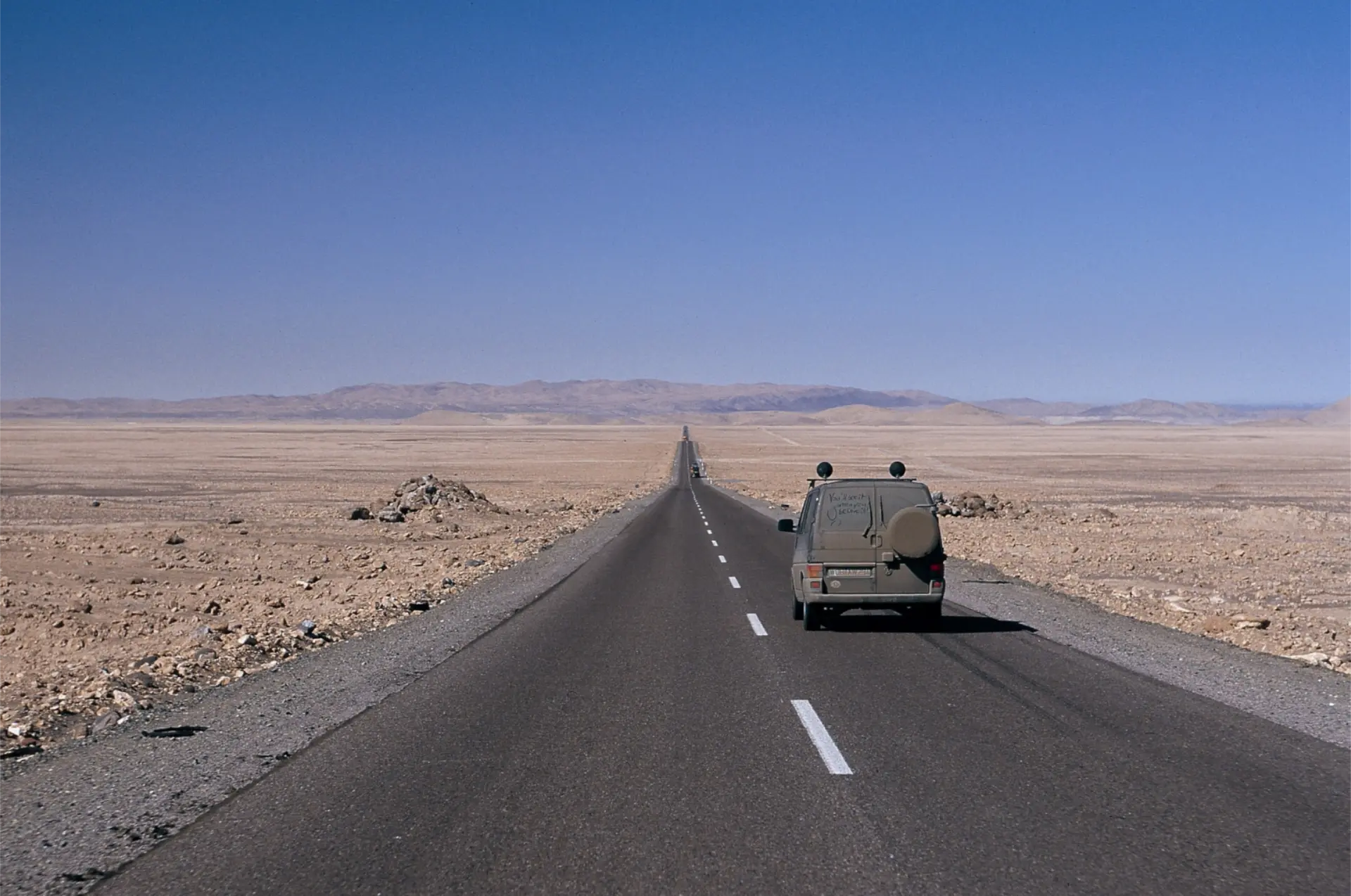 Un vehículo Volkswagen circula por un camino largo y recto a través de un paisaje desértico bajo un cielo azul claro; su tracción total proporciona una estabilidad y un control inigualables.