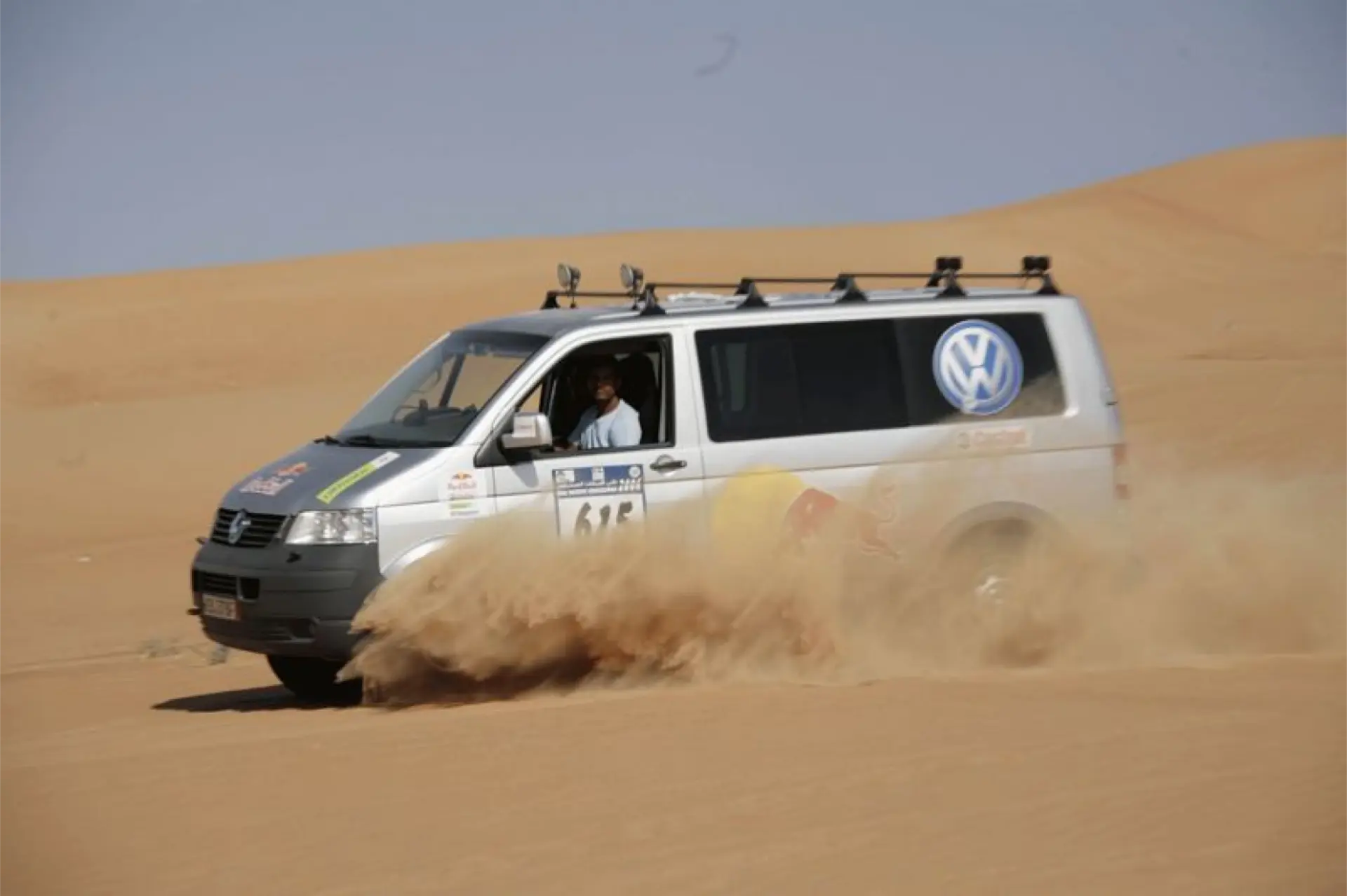Una camioneta con el icónico logotipo de Volkswagen avanza por la arena del desierto, mostrando su total tracción mientras levanta una nube de polvo.
