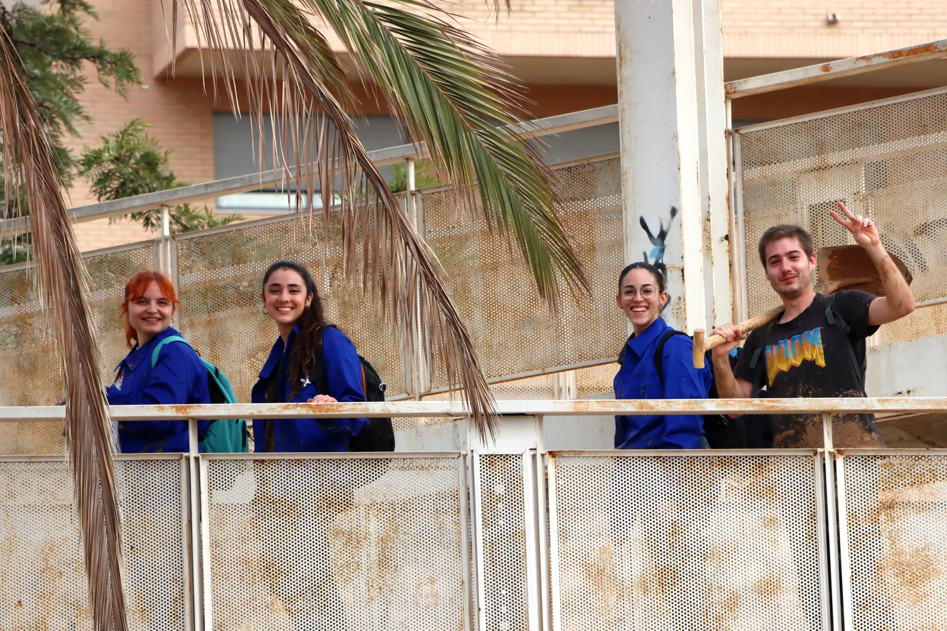 Cuatro personas subiendo las escaleras, sonrientes, tres de ellas con chaquetas azules y una haciendo el signo de la paz, un momento alegre que recuerda la camaradería en el sector del transporte.