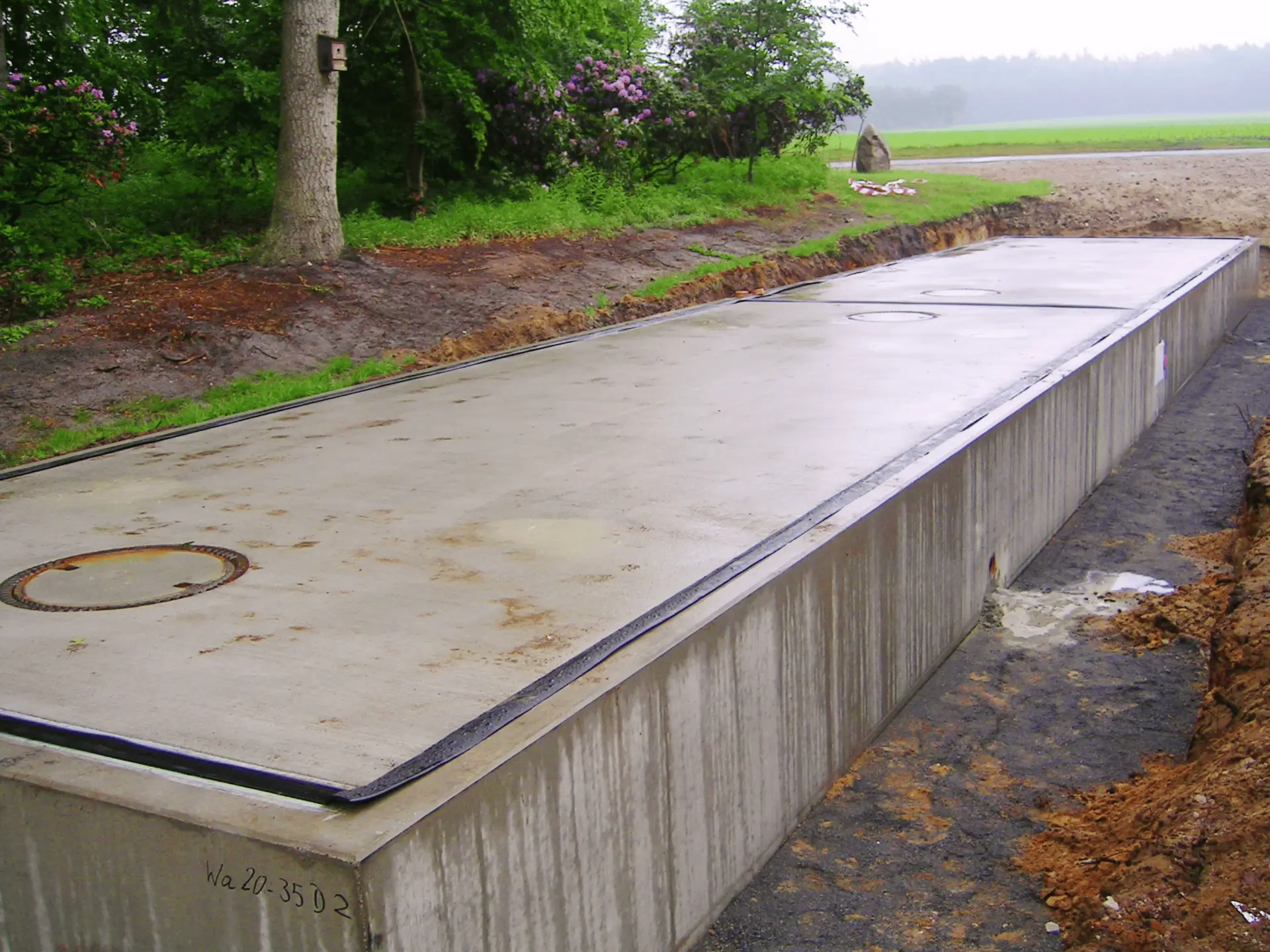 Una gran estructura rectangular de hormigón con cubiertas metálicas, el borrador automático, se encuentra al aire libre, entre árboles y zonas verdes.