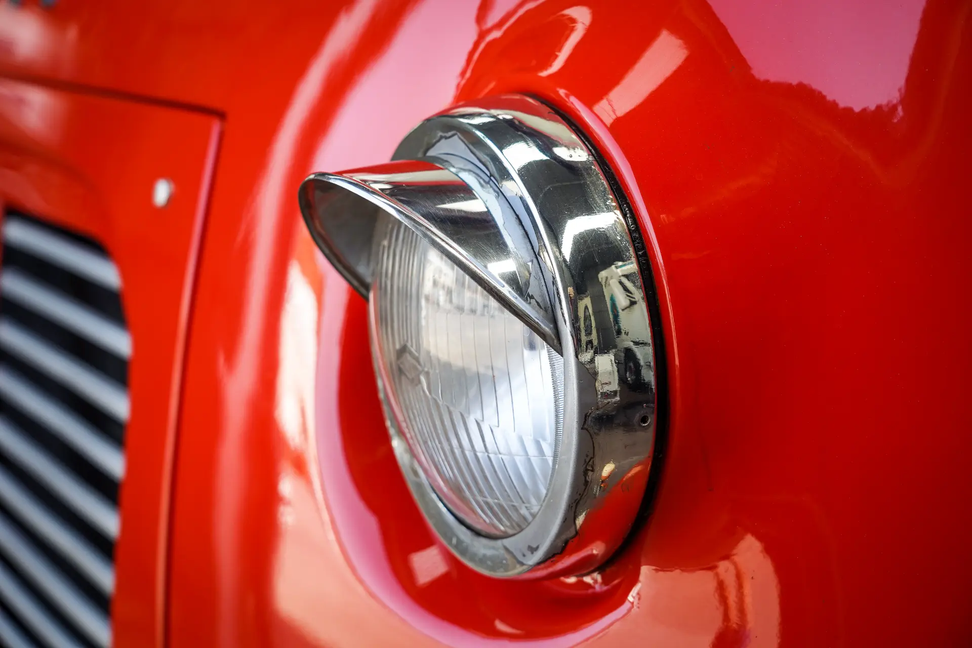 Un primer plano del faro redondo de un coche clásico con borde cromado adorna la superficie roja brillante, recordando la elegancia clásica que se encuentra en los camiones clásicos restaurados como el Avia 3500.