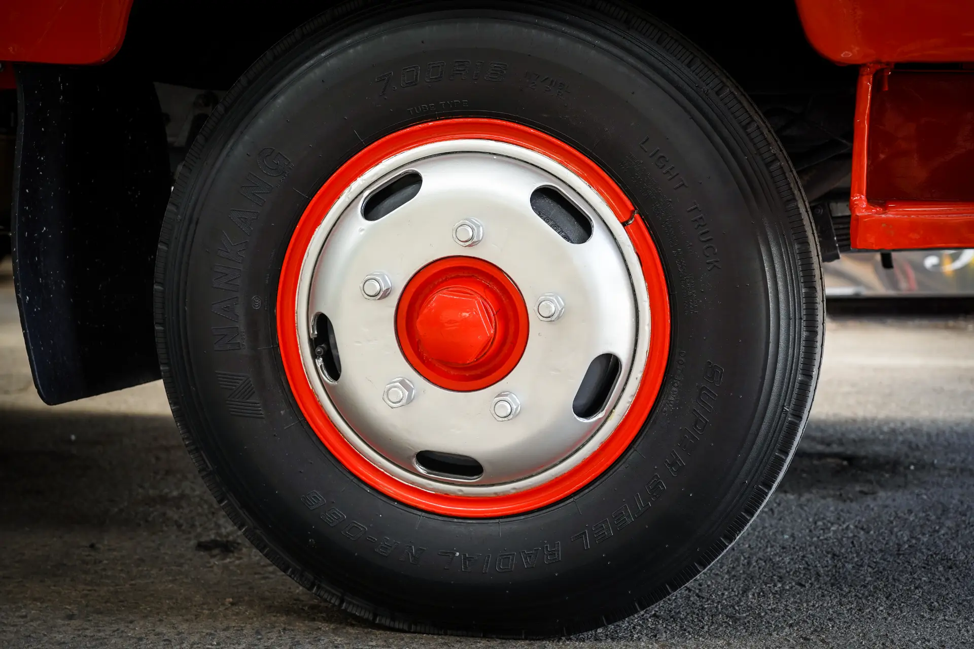 Primer plano de una rueda de camión con tapacubos rojo y neumático negro, estacionada sobre una superficie de concreto gris, parte de un proyecto de restauración del Avia 3500 que destaca los camiones clásicos restaurados.