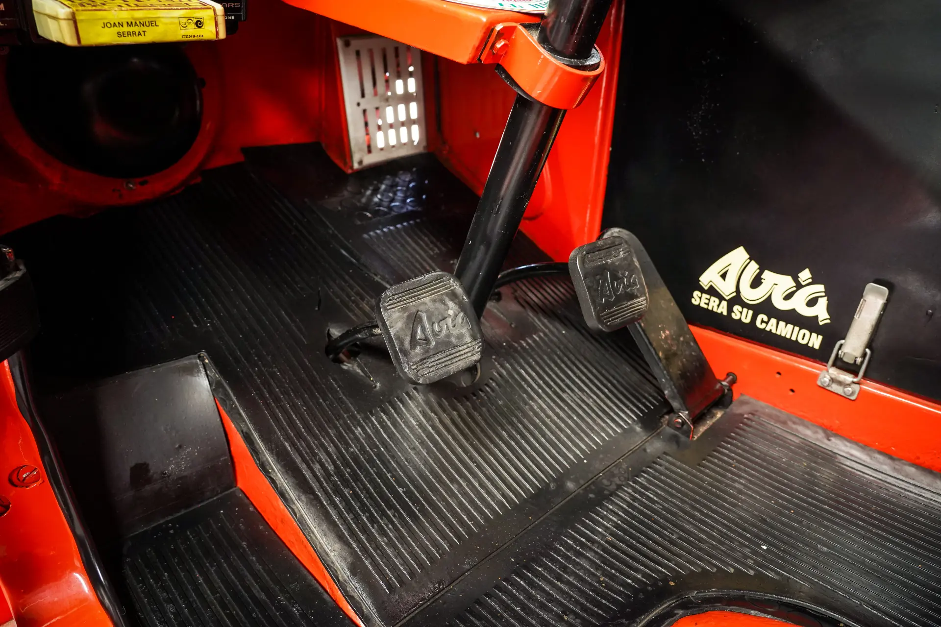 Primer plano del área de pedales de un vehículo con interior rojo y negro, con pedales de embrague y freno etiquetados "Avia 3500", que capturan la atención al detalle en esta meticulosa restauración.