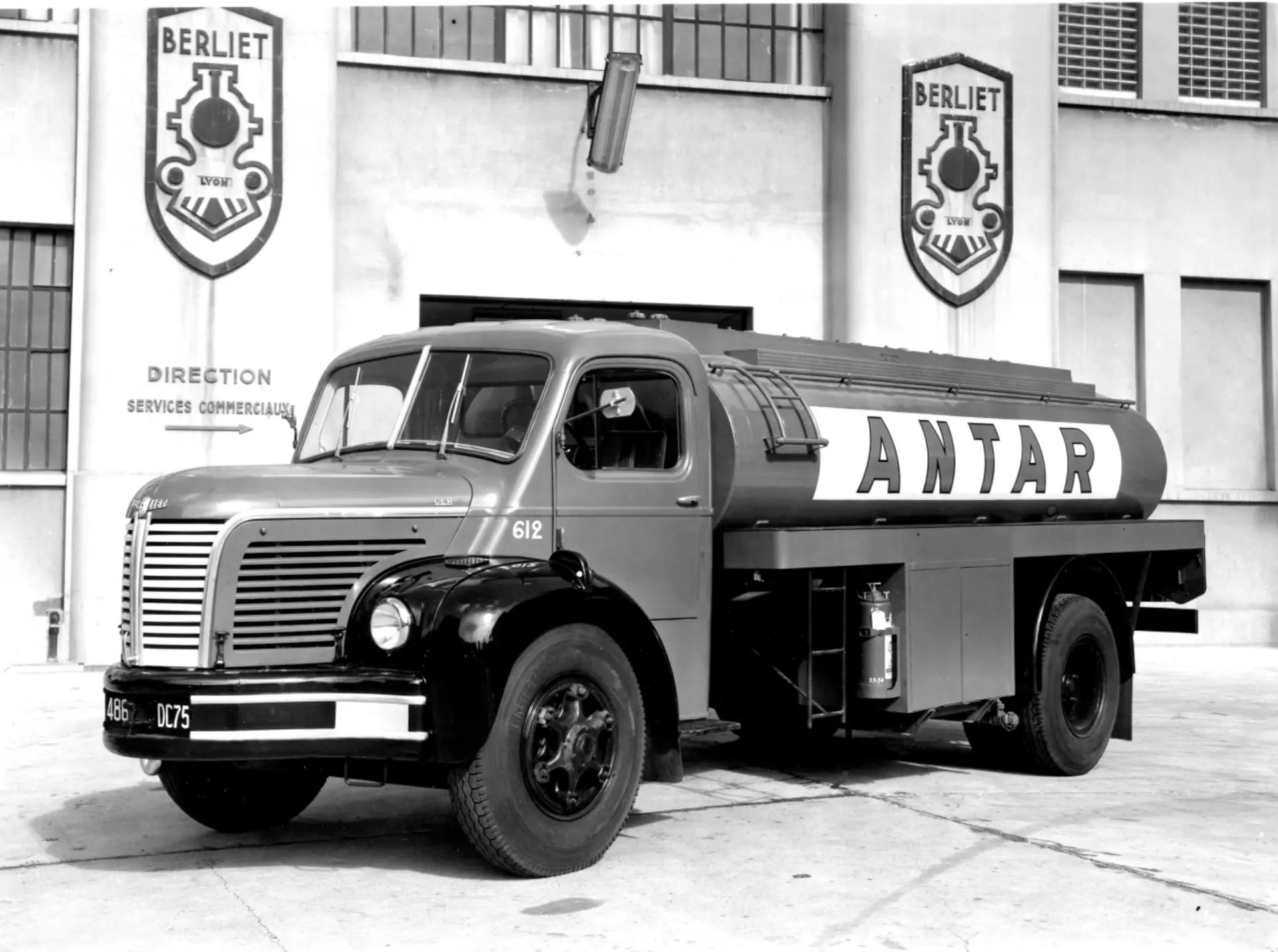 Un antiguo camión cisterna Antar, que recuerda la época anterior a la incursión de Renault en la fabricación de camiones como la serie Renault Trucks T, está estacionado frente a un edificio adornado con logotipos de Berliet.