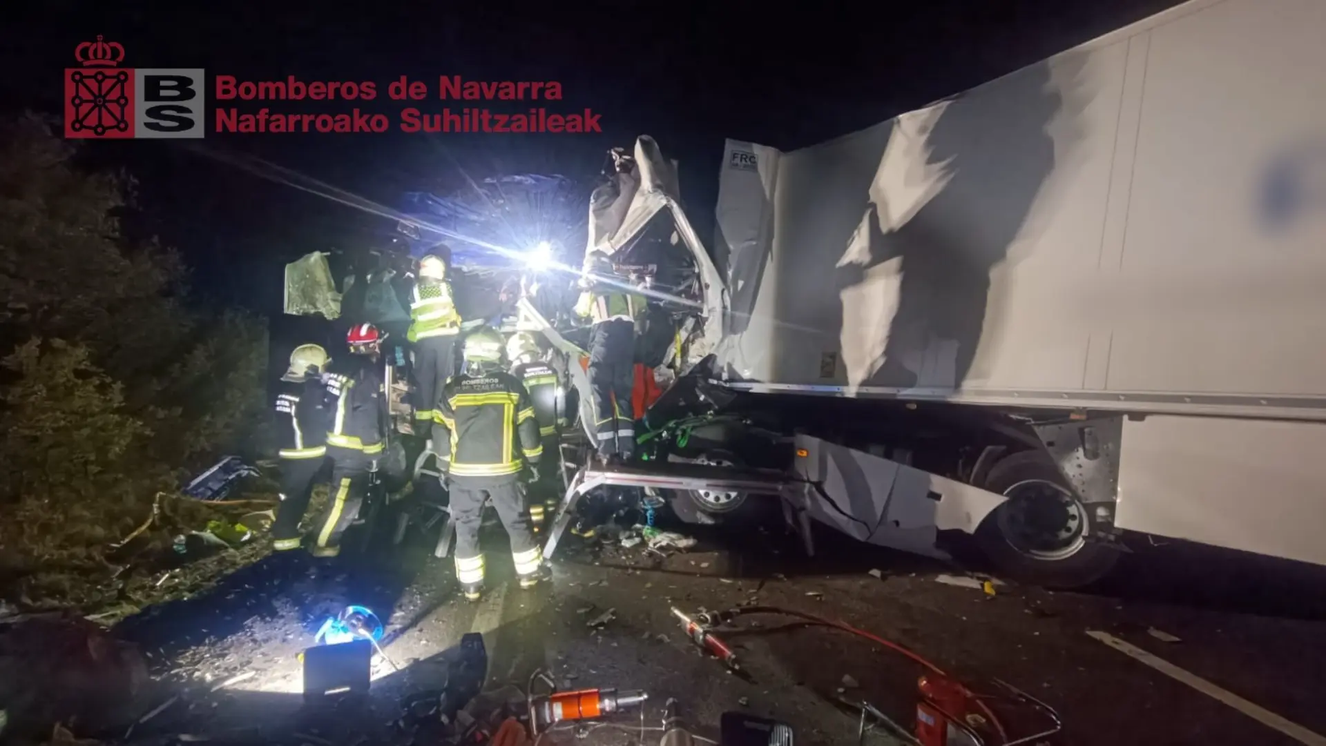 Personal de emergencias en el lugar del accidente nocturno en Fitero, con un camión y escombros esparcidos por la colisión frontal; luces brillantes iluminan la operación de rescate.