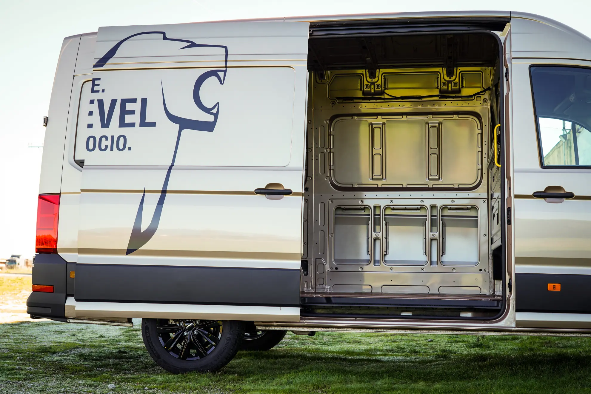 Furgoneta de carga MAN TGE 3.180 blanca con puerta lateral abierta, que muestra un espacio de almacenamiento interior vacío y limpio; logotipo visible en el exterior.