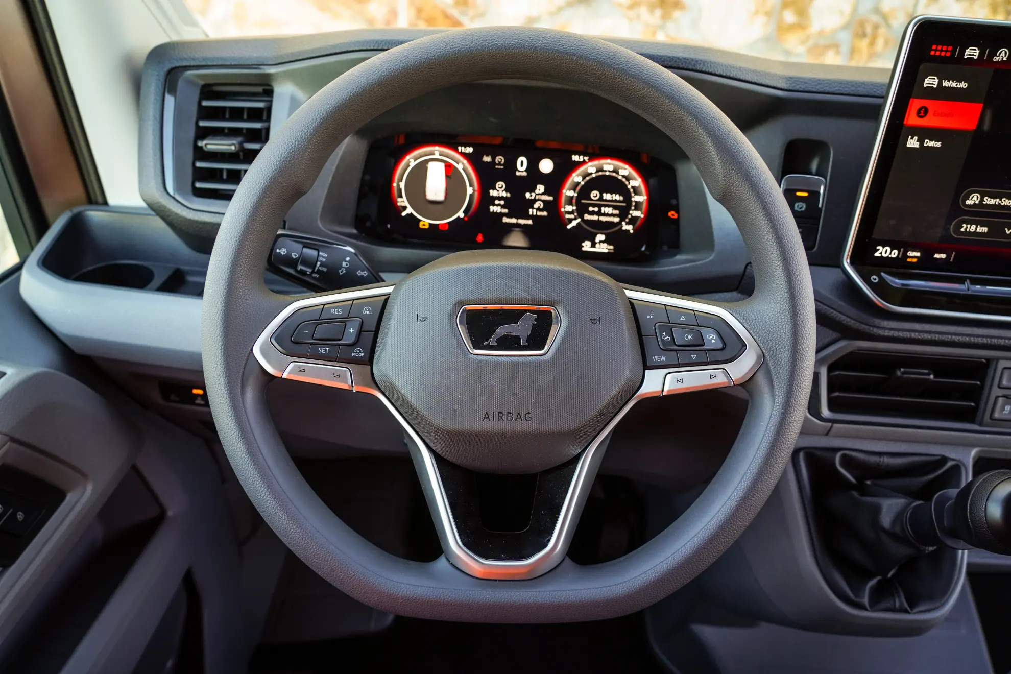 Primer plano del volante de una MAN TGE 3.180 con un tablero de instrumentos digital y una pantalla de infoentretenimiento al fondo.