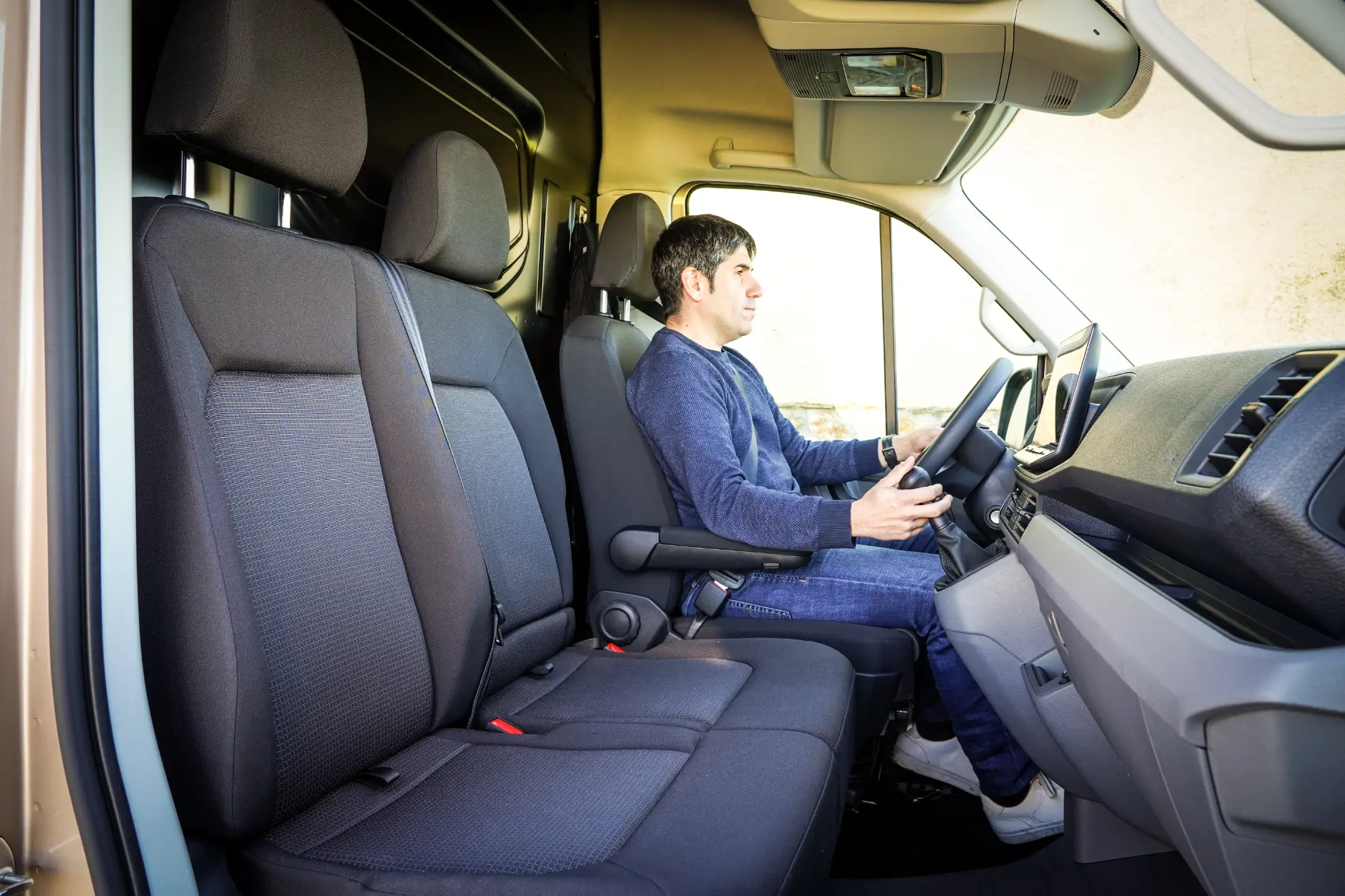 Un hombre se sienta en el asiento del conductor de una furgoneta MAN TGE 3.180, sujetando el volante con confianza, llevando claramente su conducción a otro nivel, visto desde el lado del pasajero.