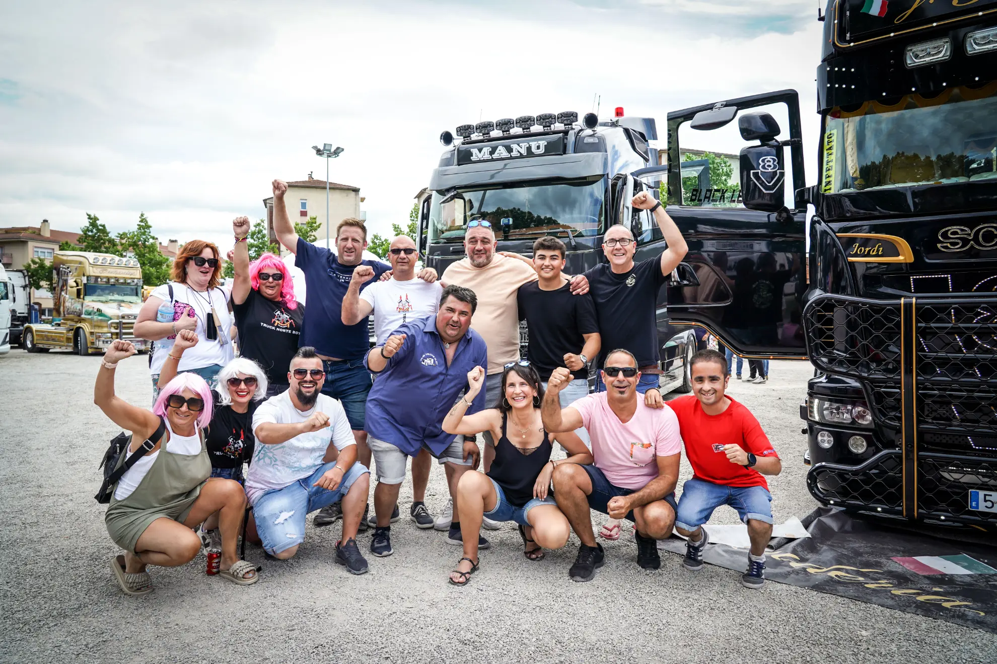 Un grupo de personas posa sonriente con los puños en alto frente a dos grandes camiones al aire libre.
