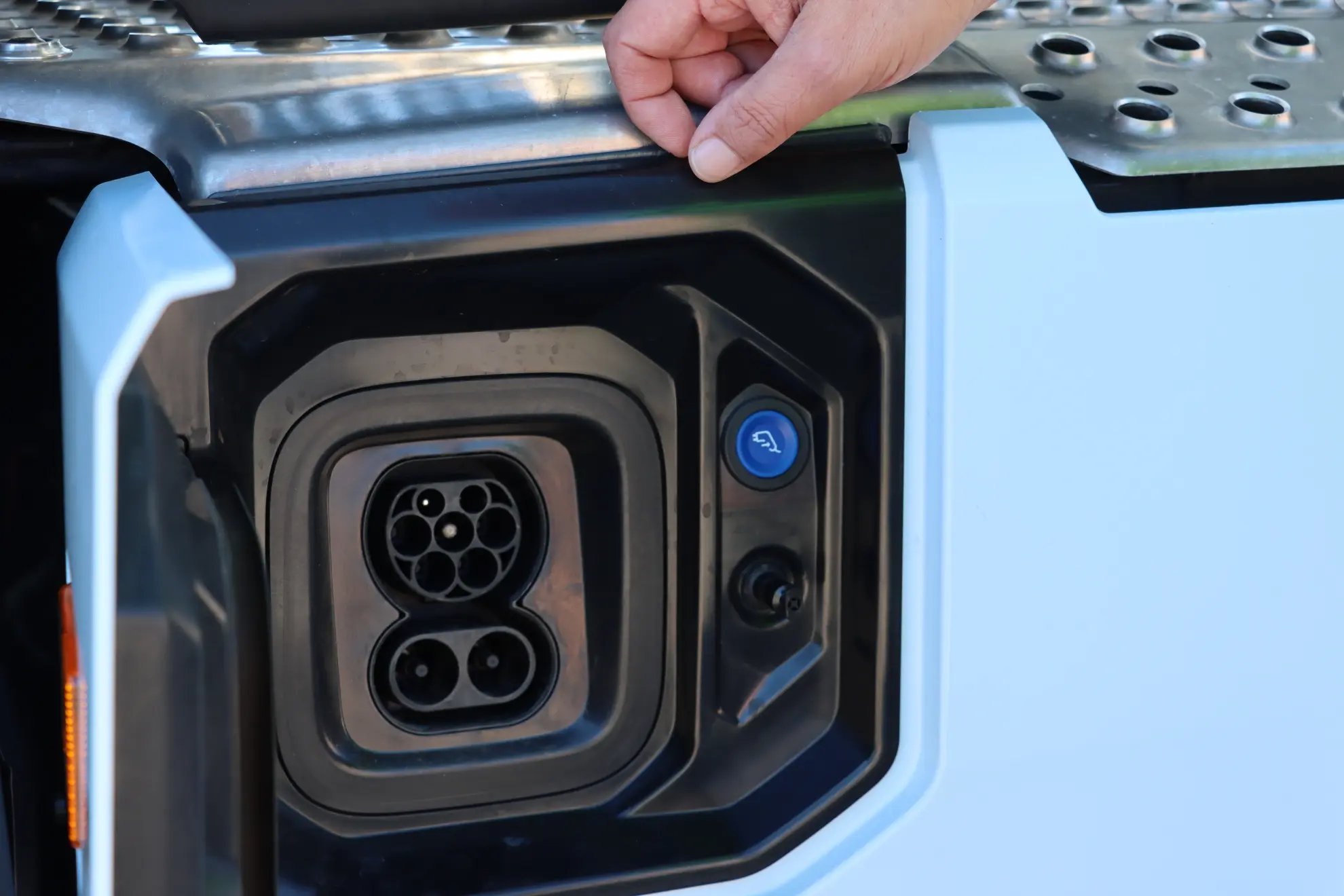 Primer plano de una mano abriendo un puerto de carga de un vehículo Eléctrico en un vehículo blanco, resaltando el cambio del diésel a soluciones sustentables como el Scania 45R.