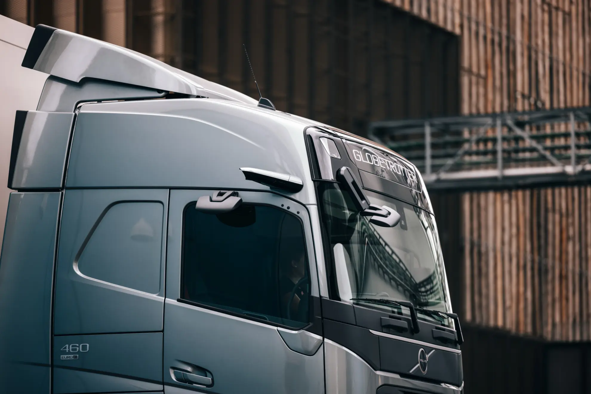 Primer plano de la cabina de un moderno camión semirremolque Volvo plateado estacionada cerca de un gran edificio industrial.