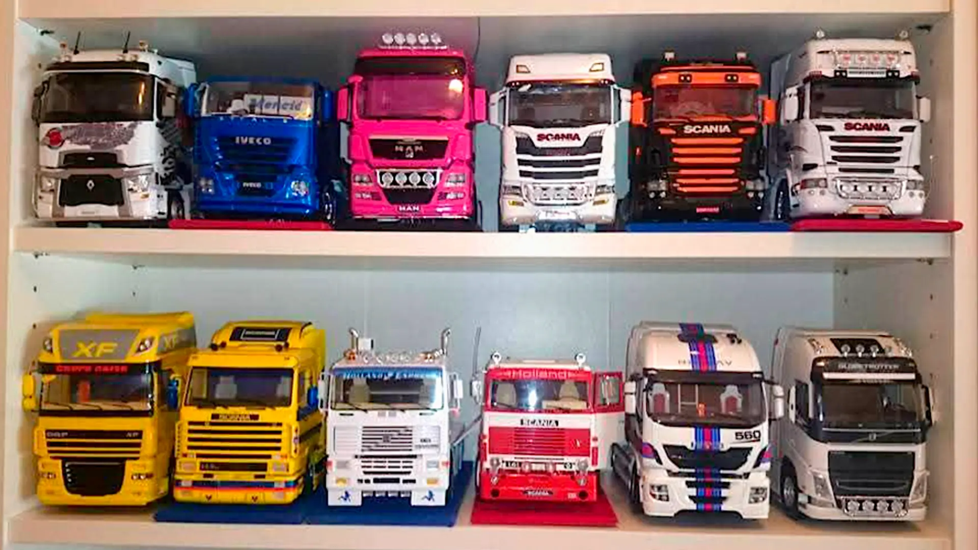 Camiones modelo de varios colores y marcas se exhiben en dos estantes en un mueble blanco, junto a un Borrador automático.